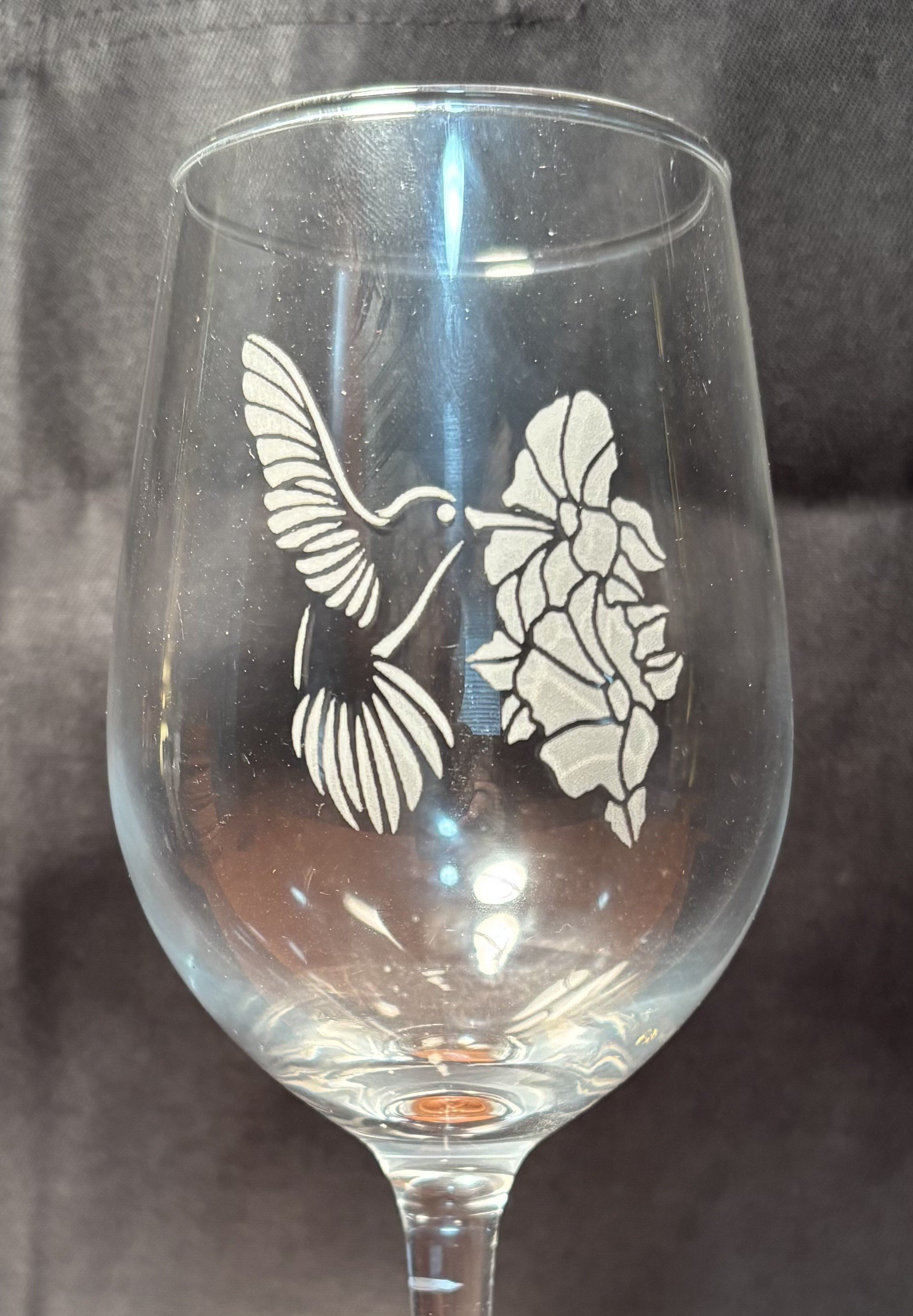 A wine glass with a decorative etching of a hummingbird near flowers on its surface.