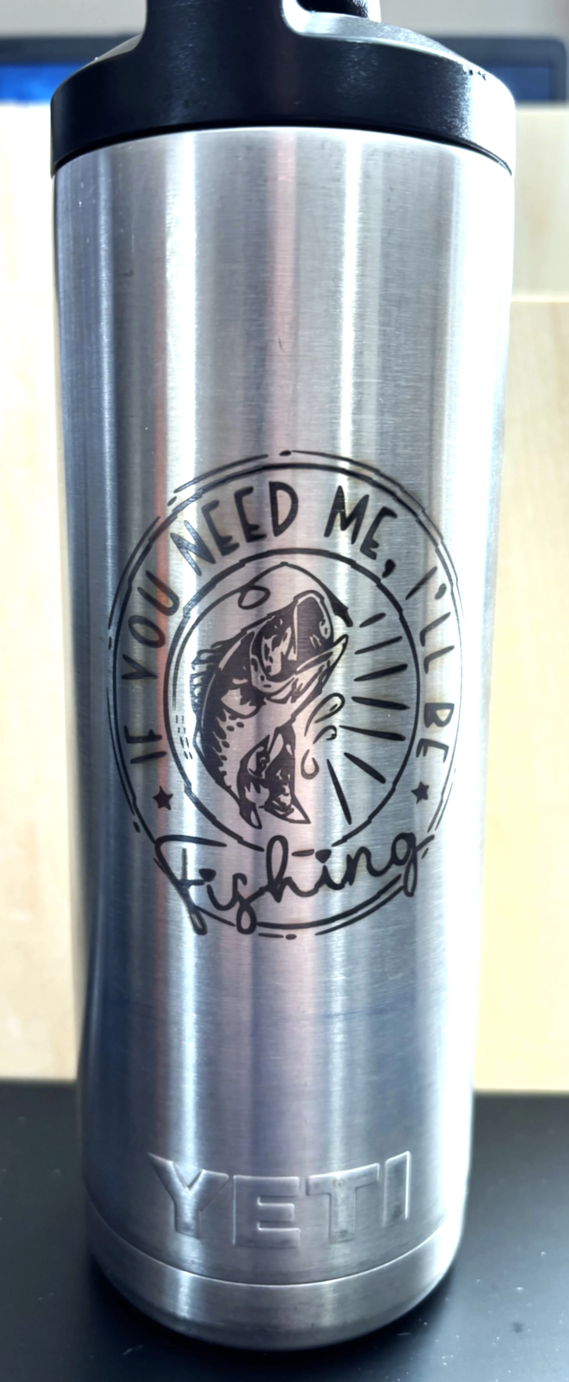A stainless steel YETI tumbler with a black lid, featuring a decal of a fish and the words "If you need me, I be fishing."