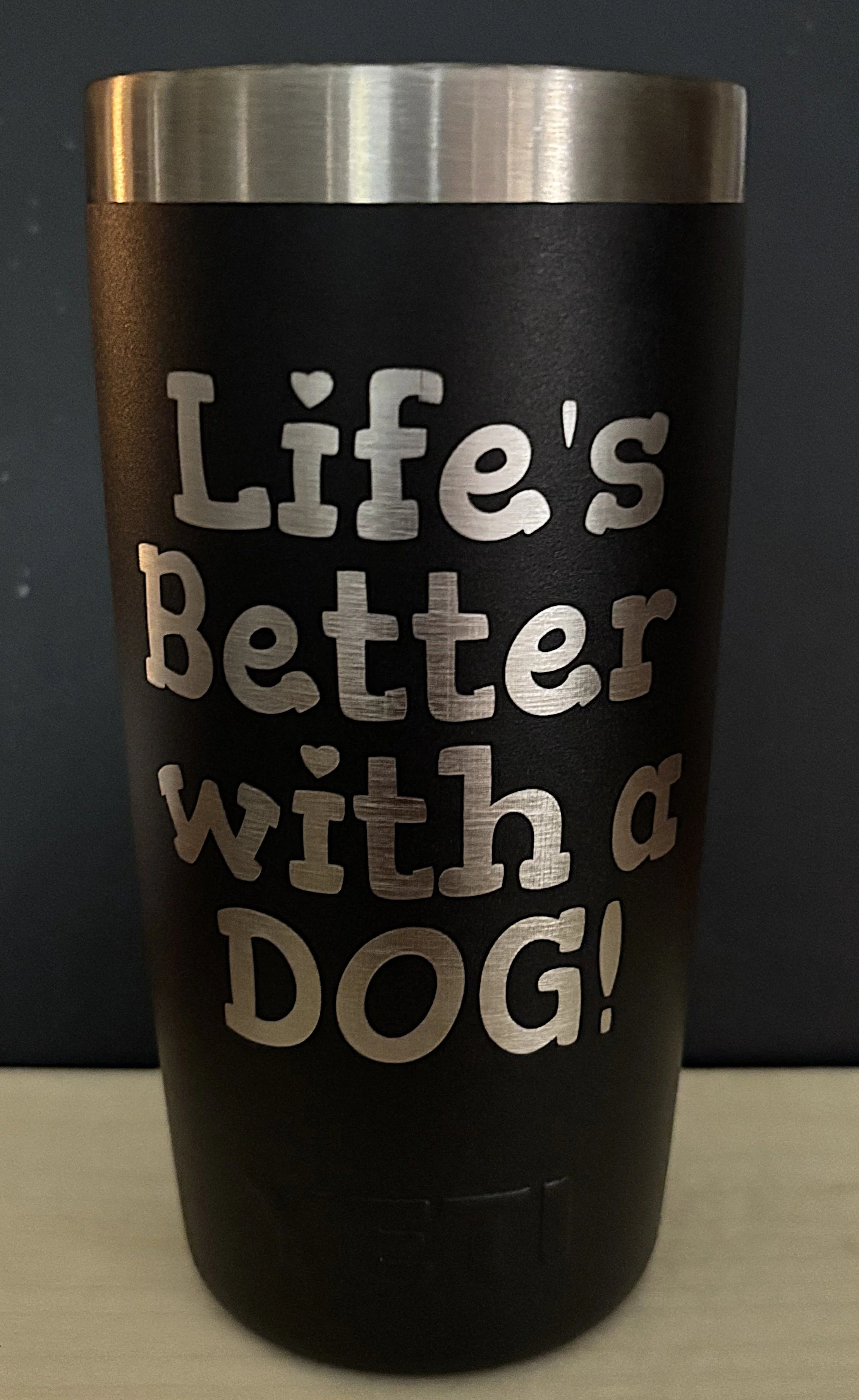 A black tumbler with silver lettering that reads "Life's Better with a Dog!" and a silver lid.