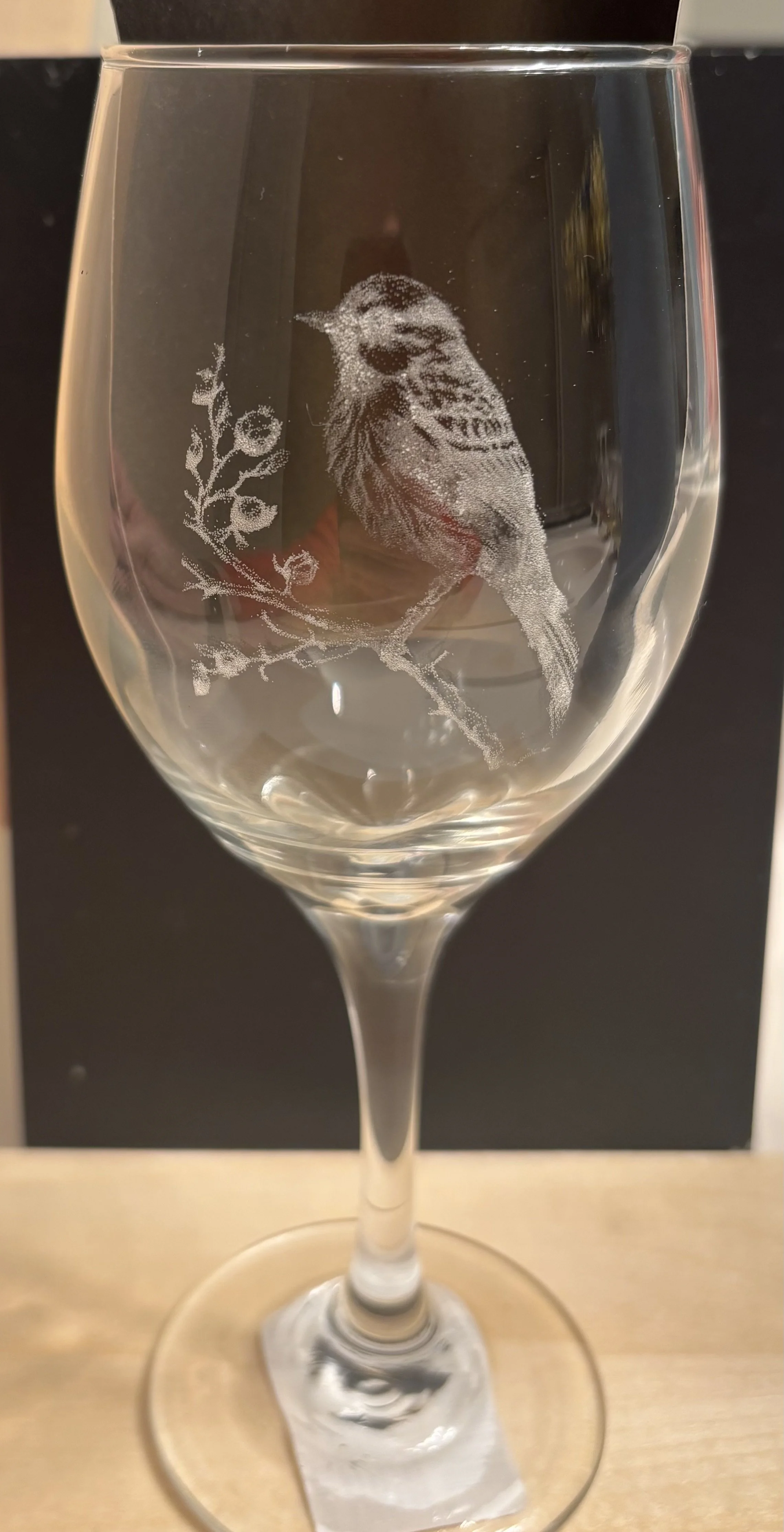 A wine glass with an etched design of a bird perched on a branch with leaves.