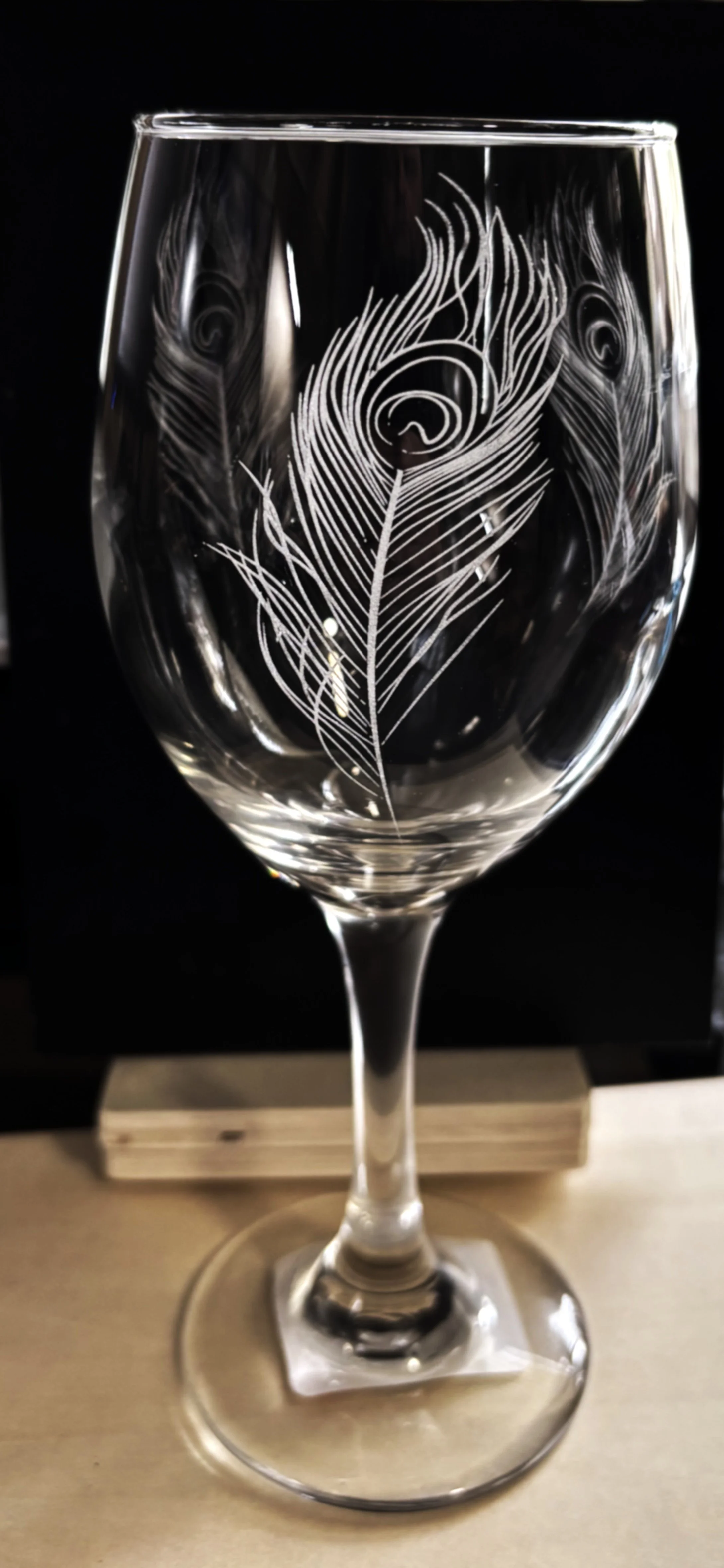 A clear wine glass with an etched peacock feather design.