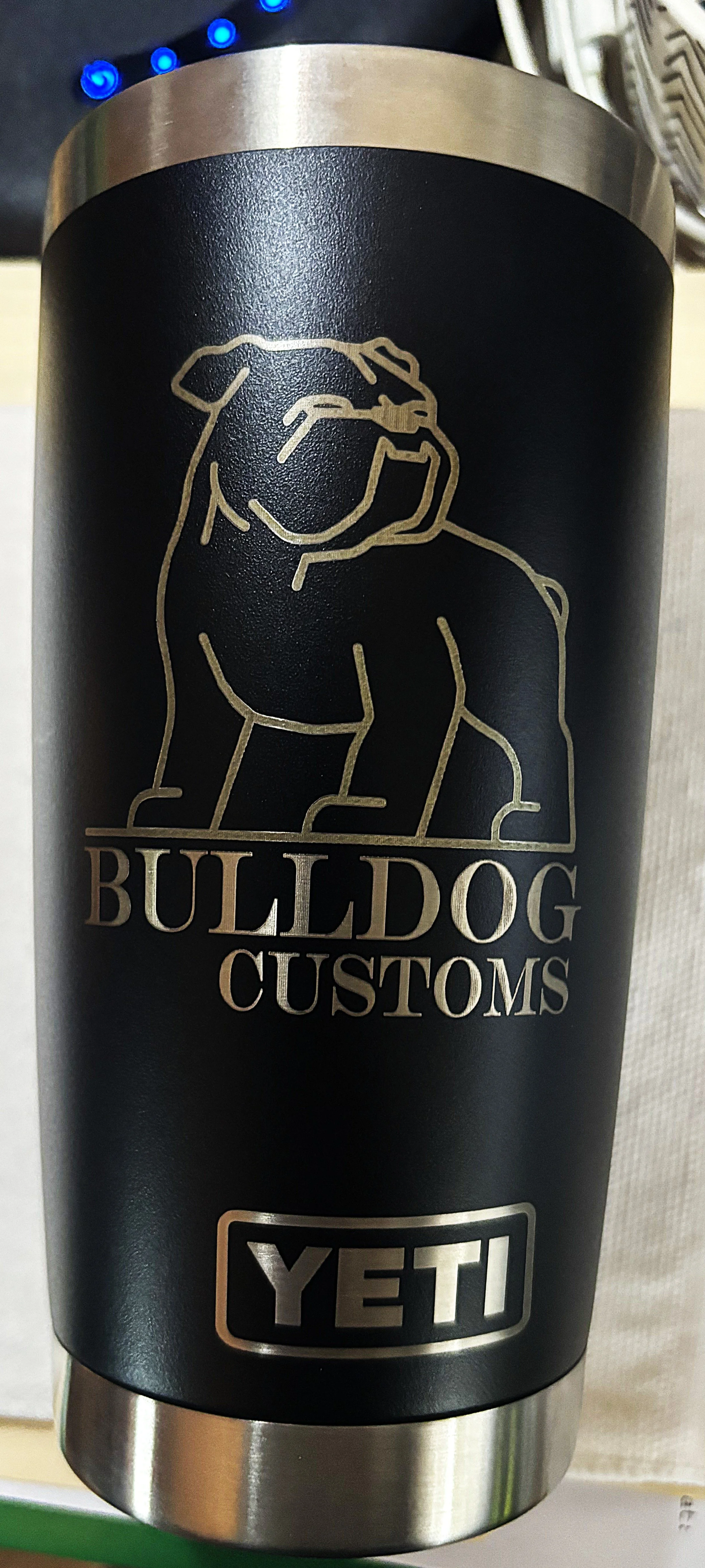 A black YETI tumbler with silver accents displaying a logo and text. The logo features a line drawing of a bulldog and the words 'BULLDOG CUSTOMS'. The YETI brand logo is at the bottom in a rectangular outline.