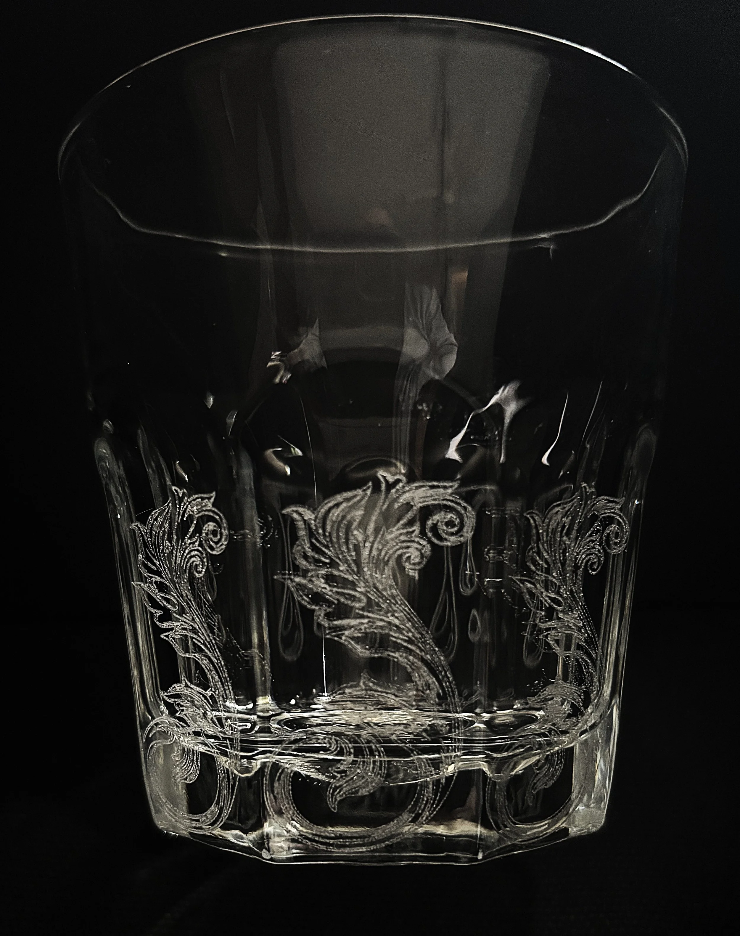 A clear glass with decorative engravings filled partially with dark liquid, set against a black background.
