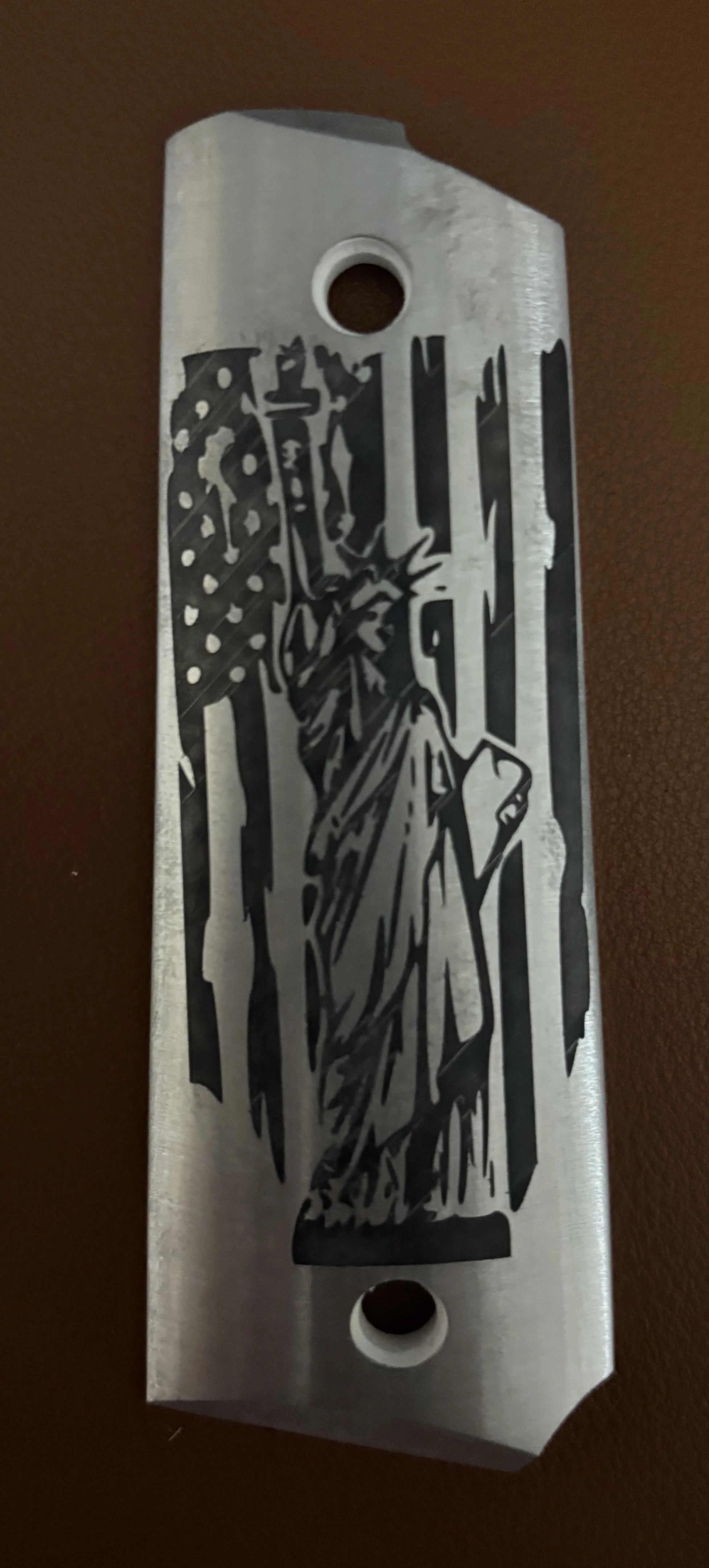 A metal blade with an engraved image of the Statue of Liberty and an American flag background.