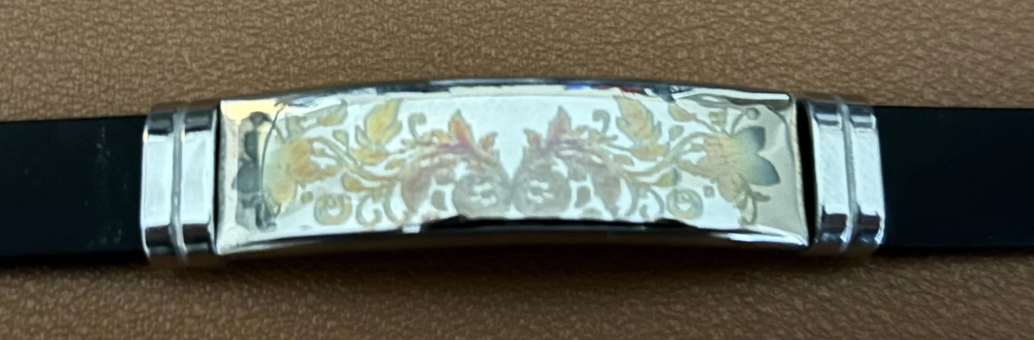 A black leather belt with a metal buckle, which has an ornamental design featuring two lions' heads surrounded by floral and vine patterns.