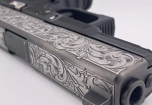 Close-up of a handgun with intricate decorative engravings on the slide.