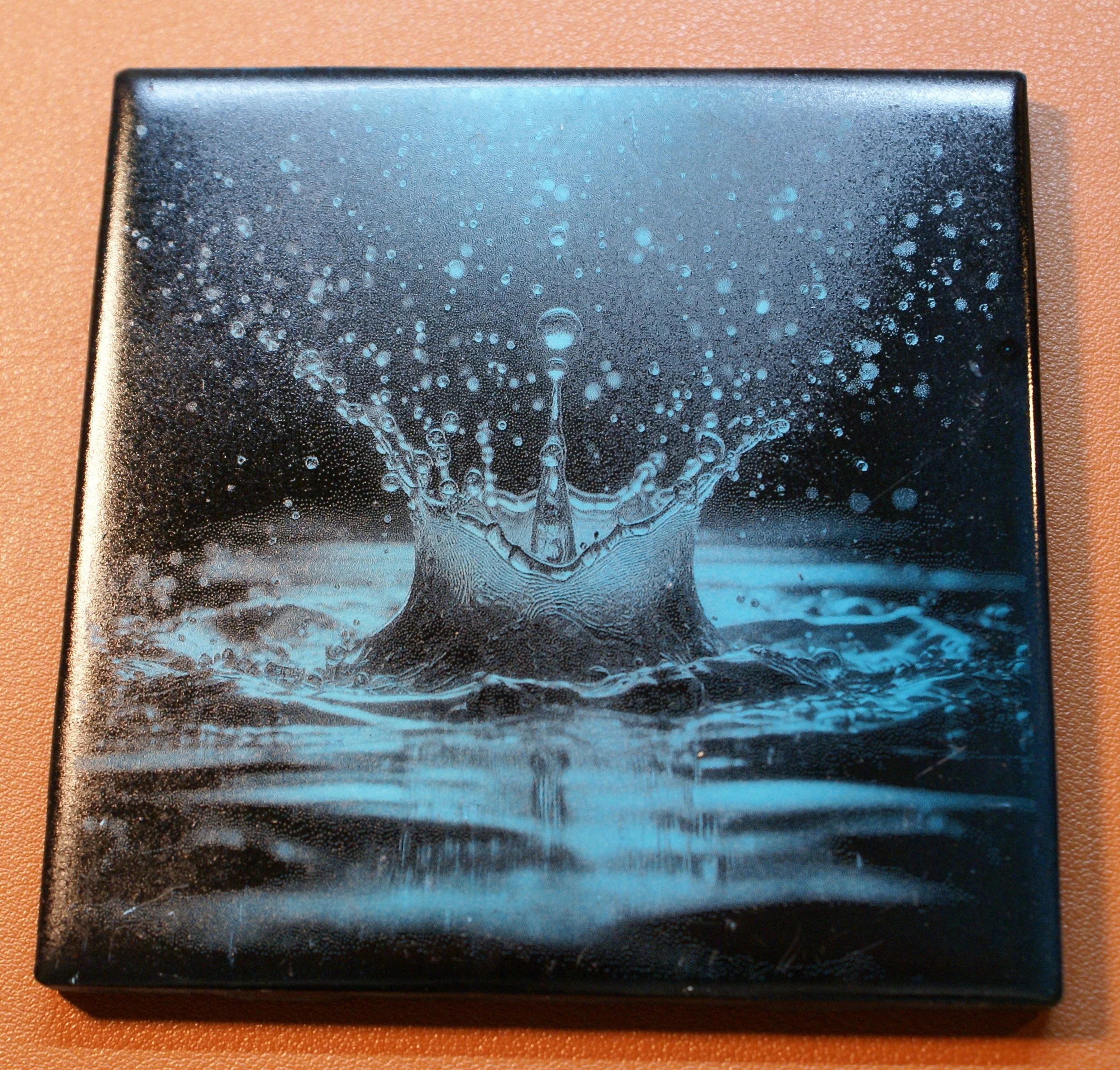 Close-up of a black box with a blue water splash illustration on top, showing water droplets and ripples.