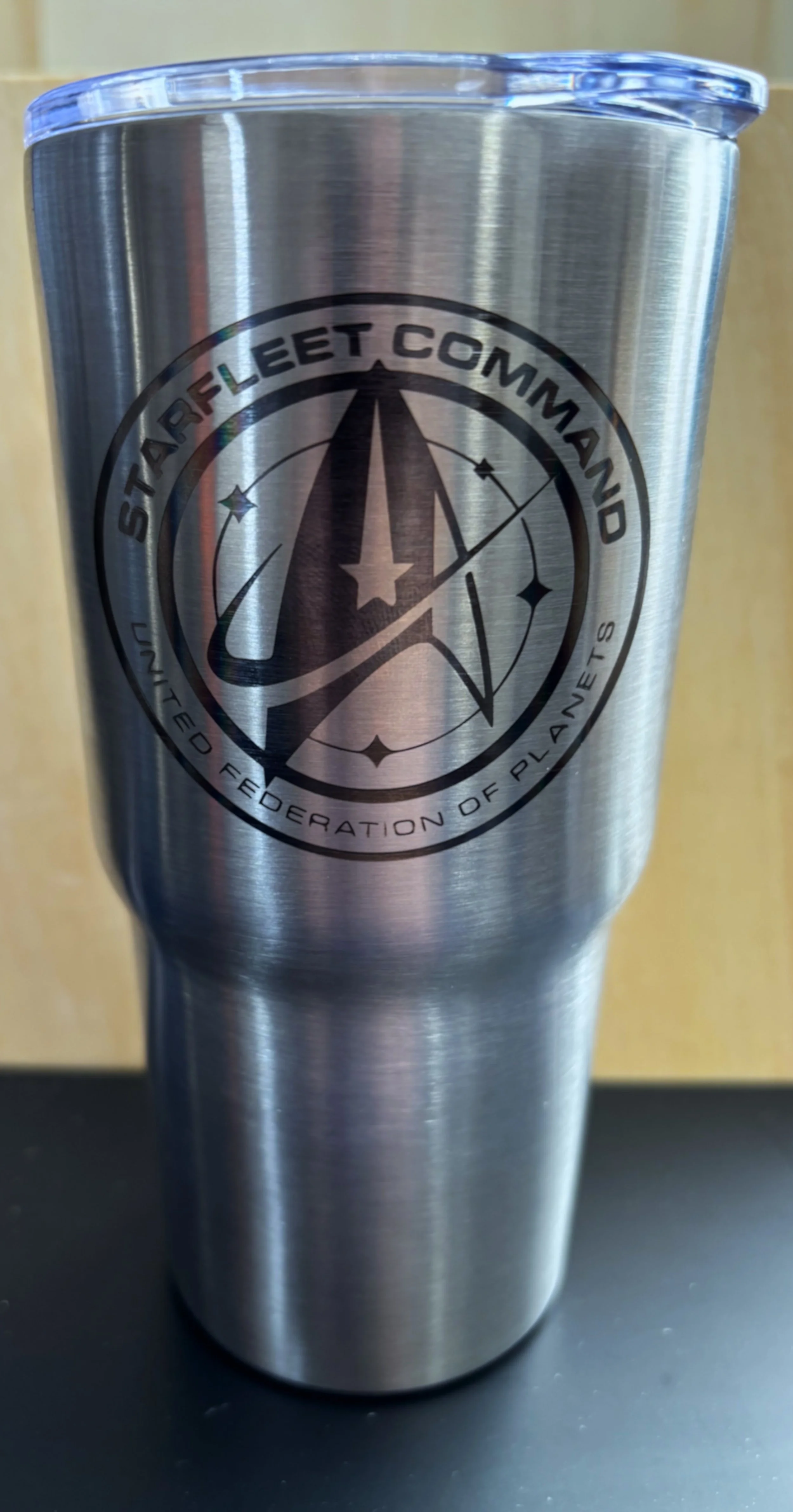 A stainless steel tumbler with a Starfleet Command emblem from Star Trek, featuring a black circular logo with a star and starship design.