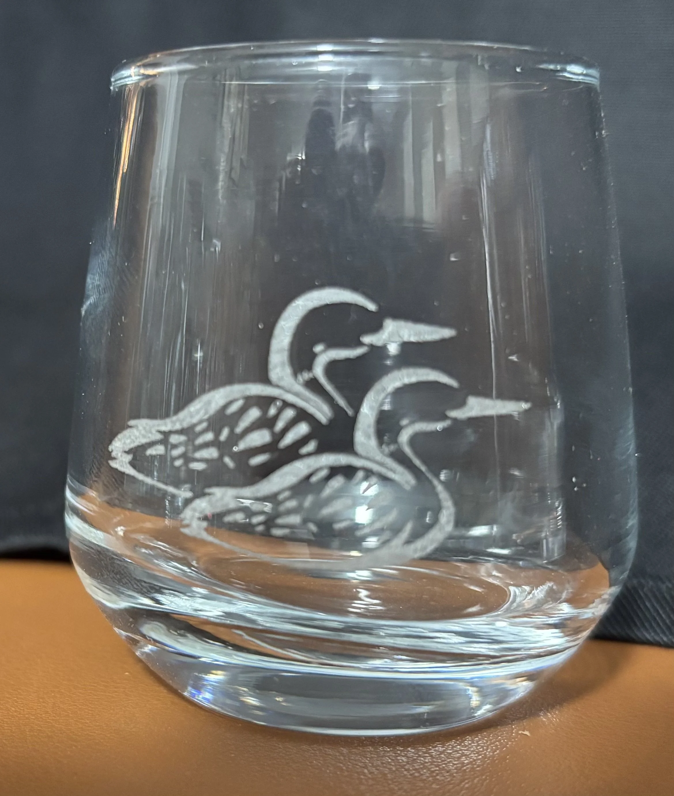 Clear water glass with an etched design of two egrets or herons on the side, placed on an orange surface with a dark background.
