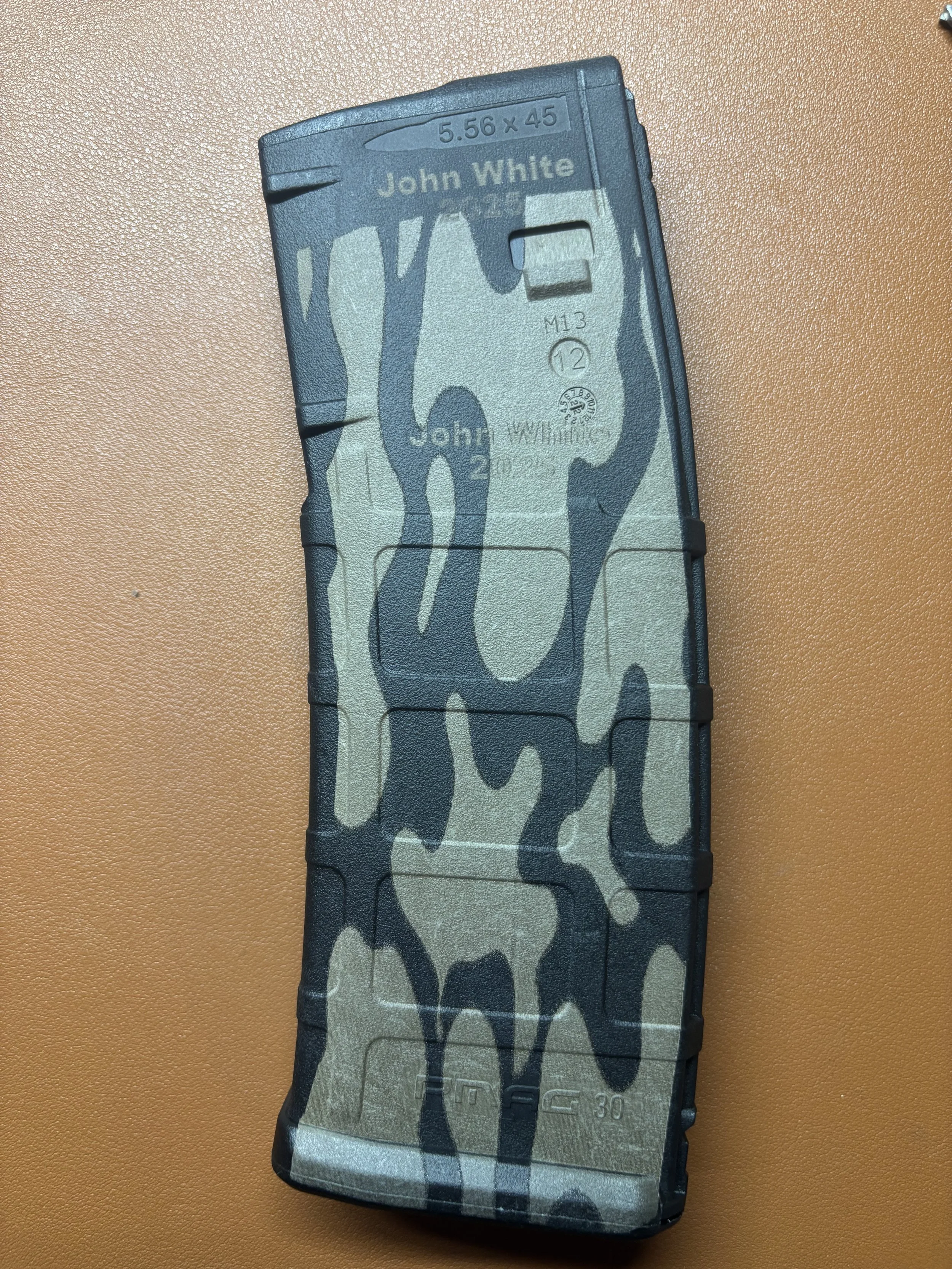 Camouflage-patterned rifle magazine on a tan surface.