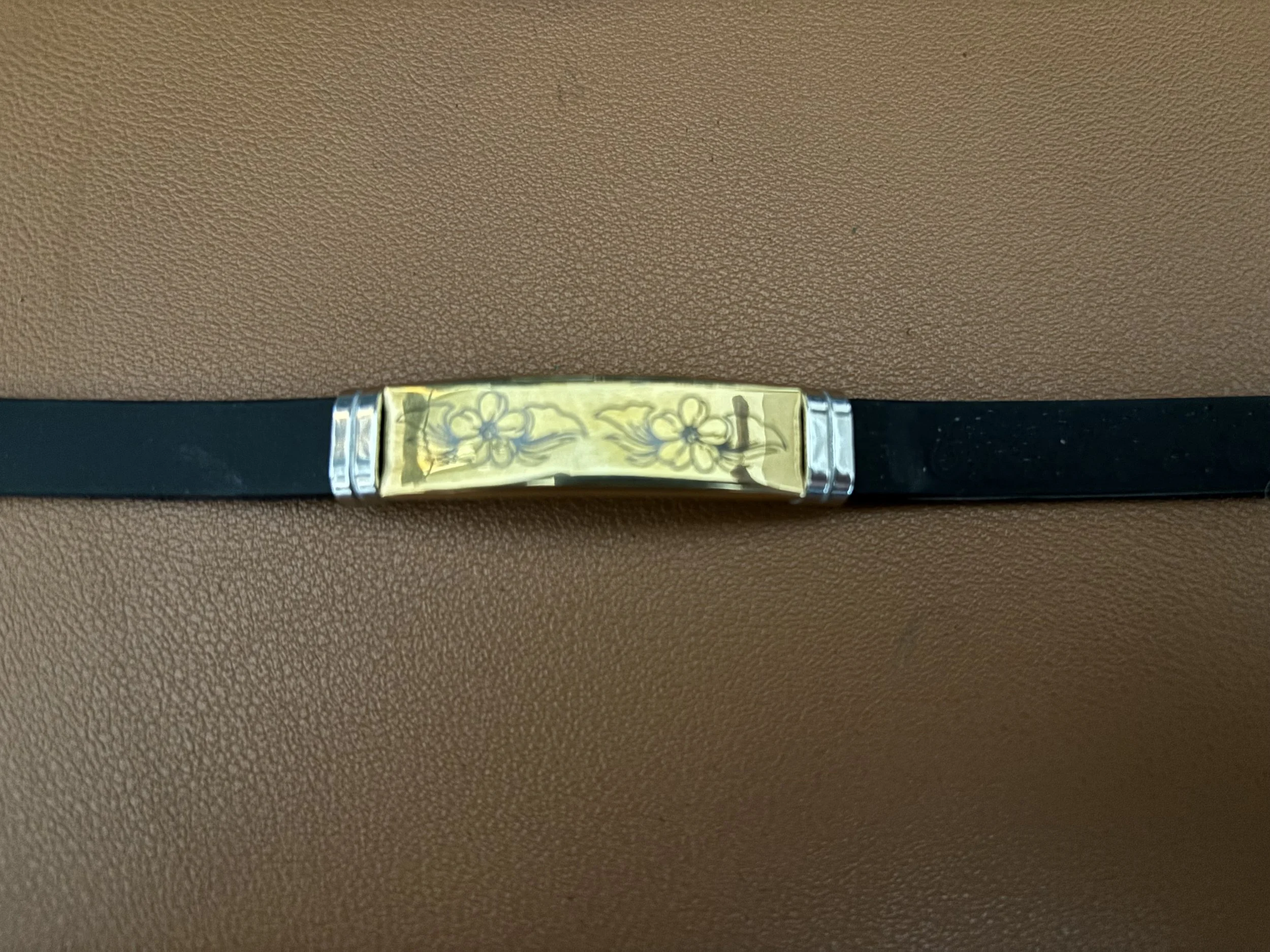 A black belt with a shiny, gold-colored buckle engraved with floral patterns, laid on a brown textured surface.