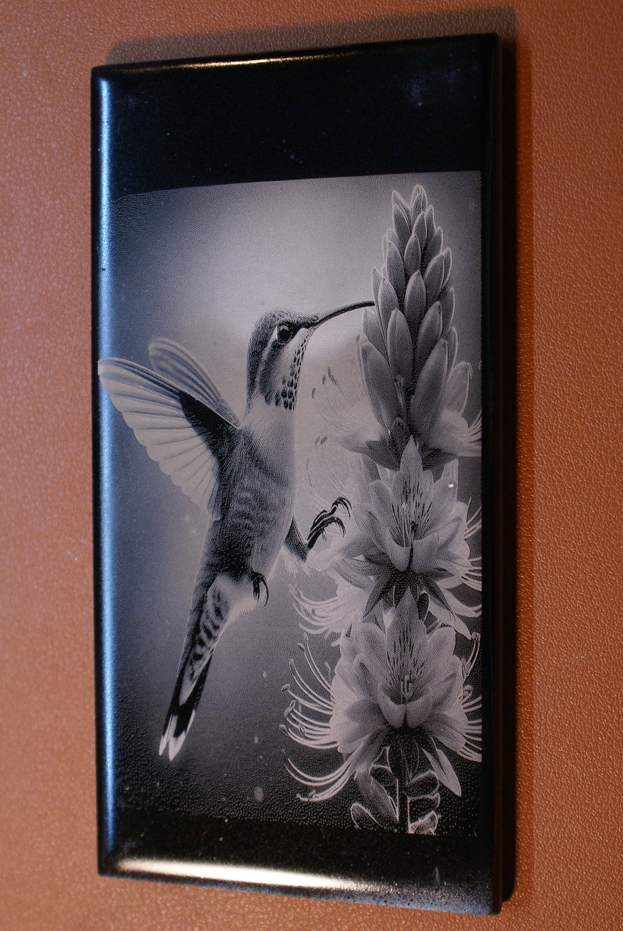 Black and white painting of a hummingbird feeding from a tall flower, mounted on a wall.