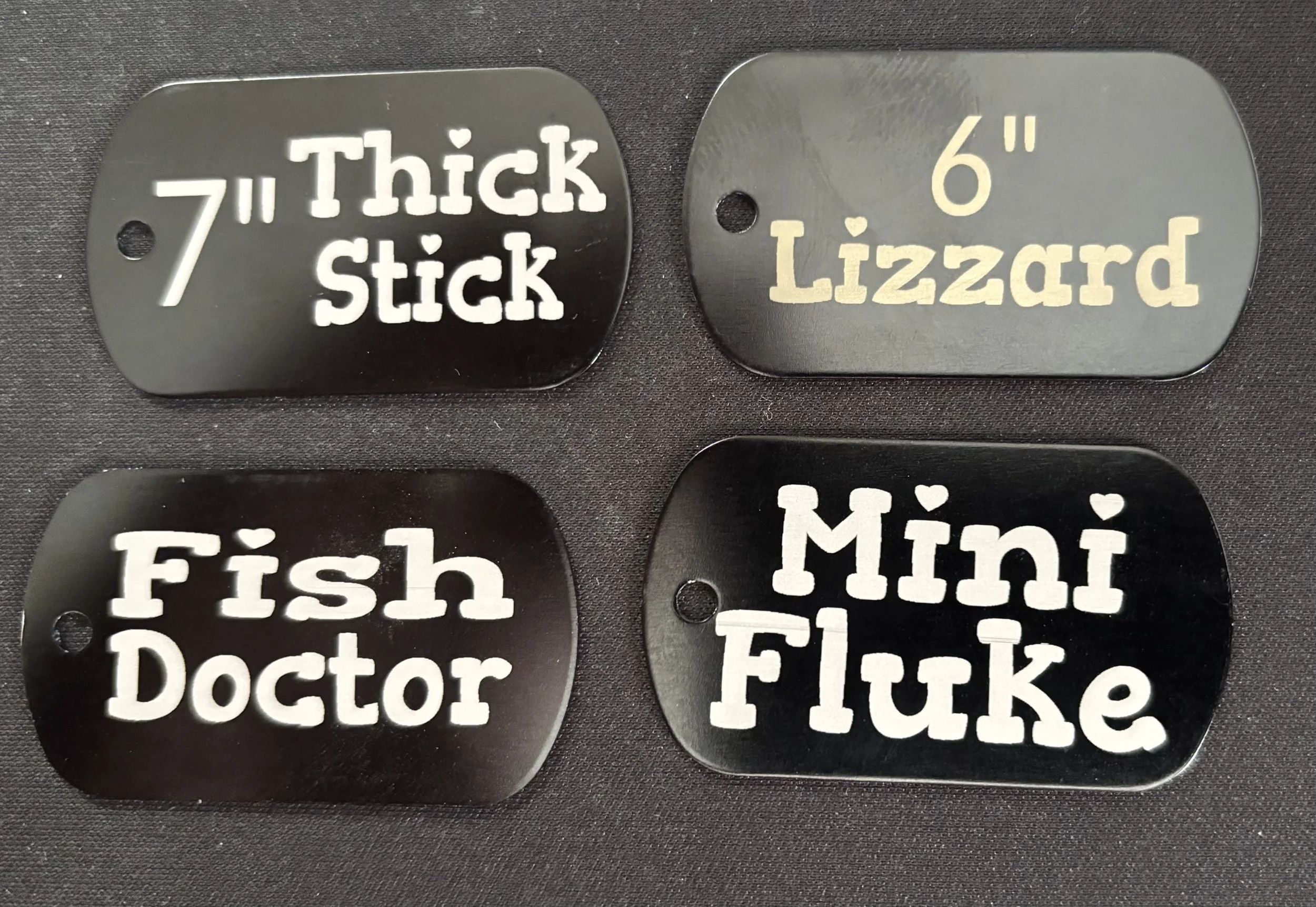 Four black dog tags with various labels and sizes.