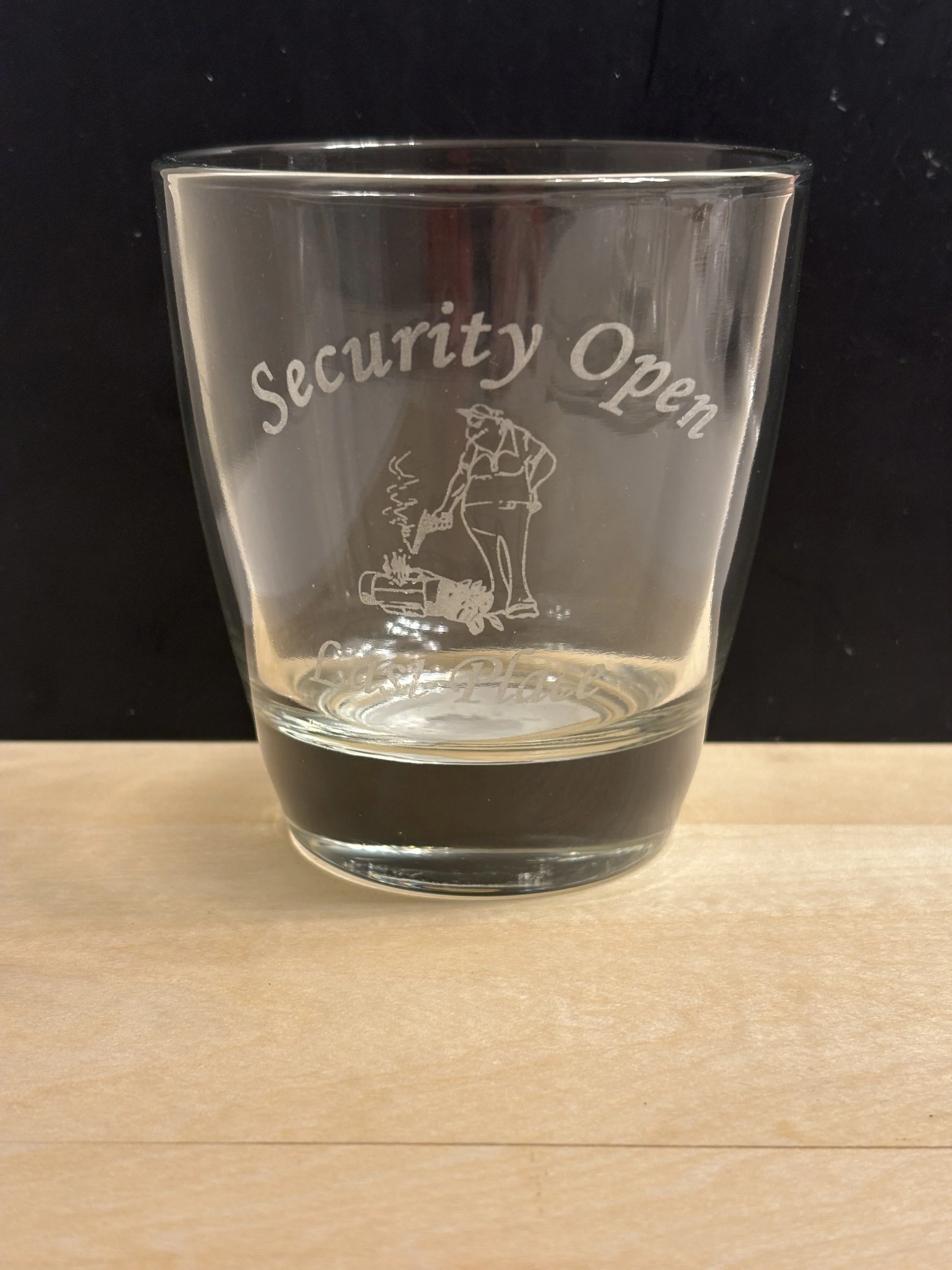 A glass with the words 'Security Open' and a cartoon drawing of a person pushing a crate with smoke coming out, set against a black background and placed on a light wood surface.