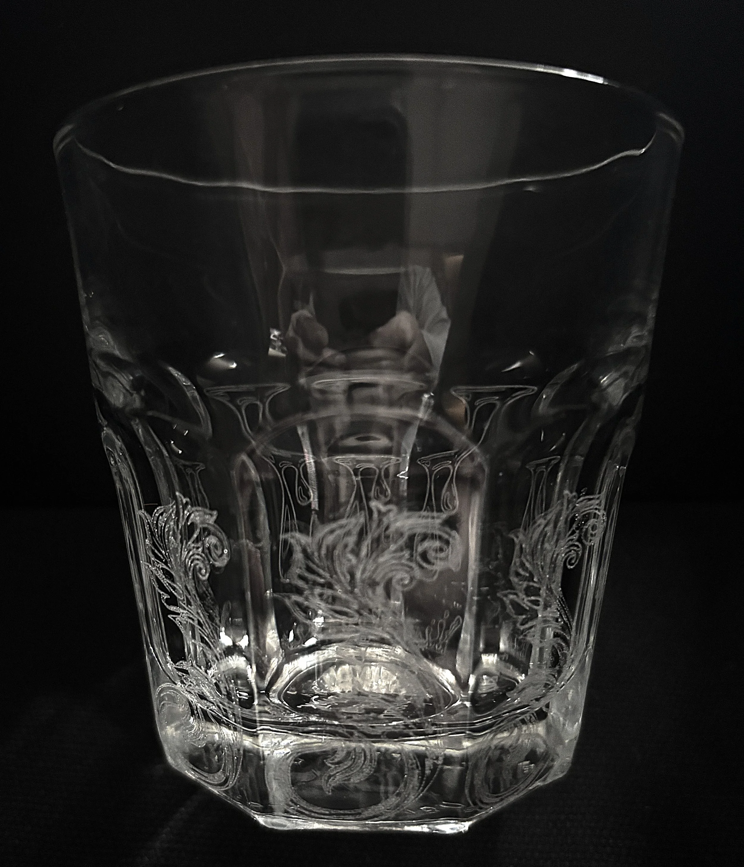 A clear glass with intricate etched designs on a black background.