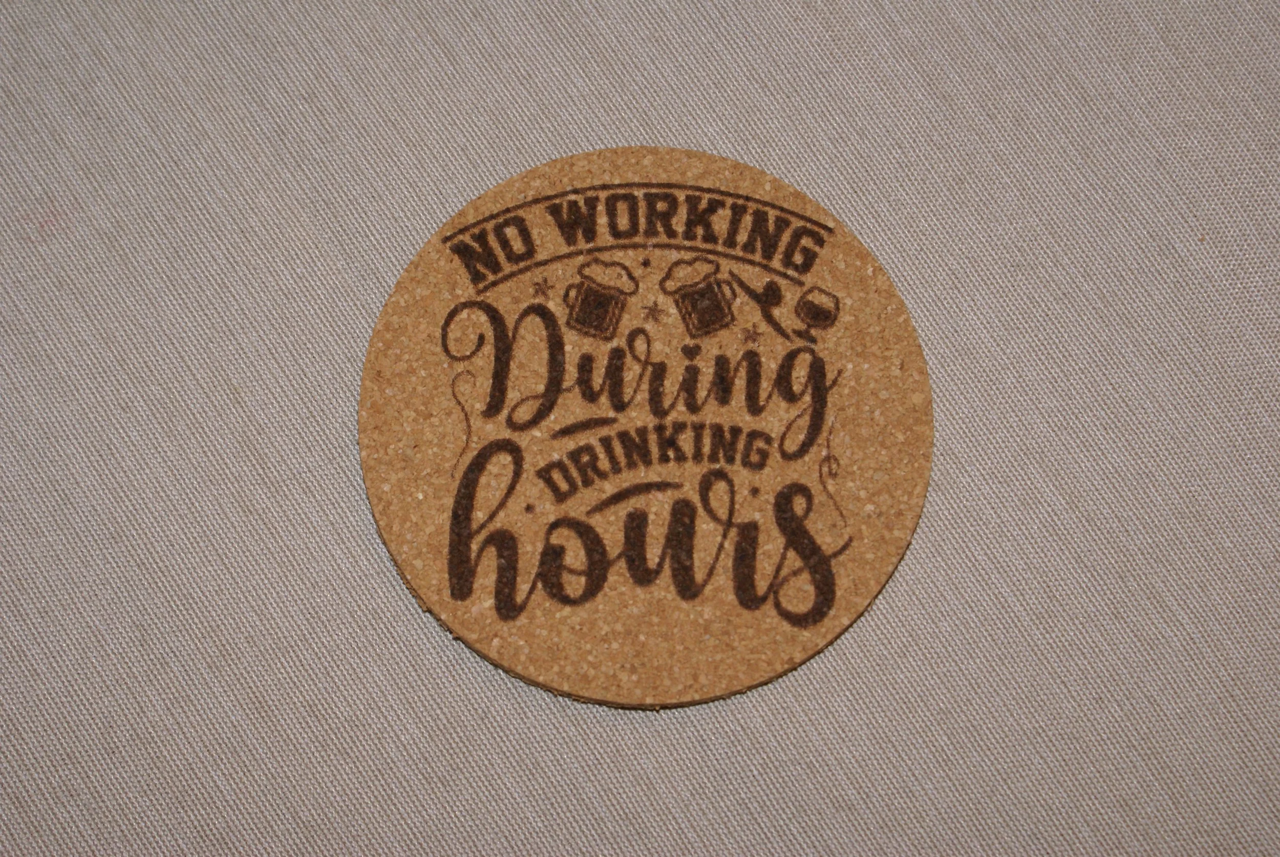 Round cork coaster with the phrase 'No working during drinking hours' and illustrations of beer mugs.