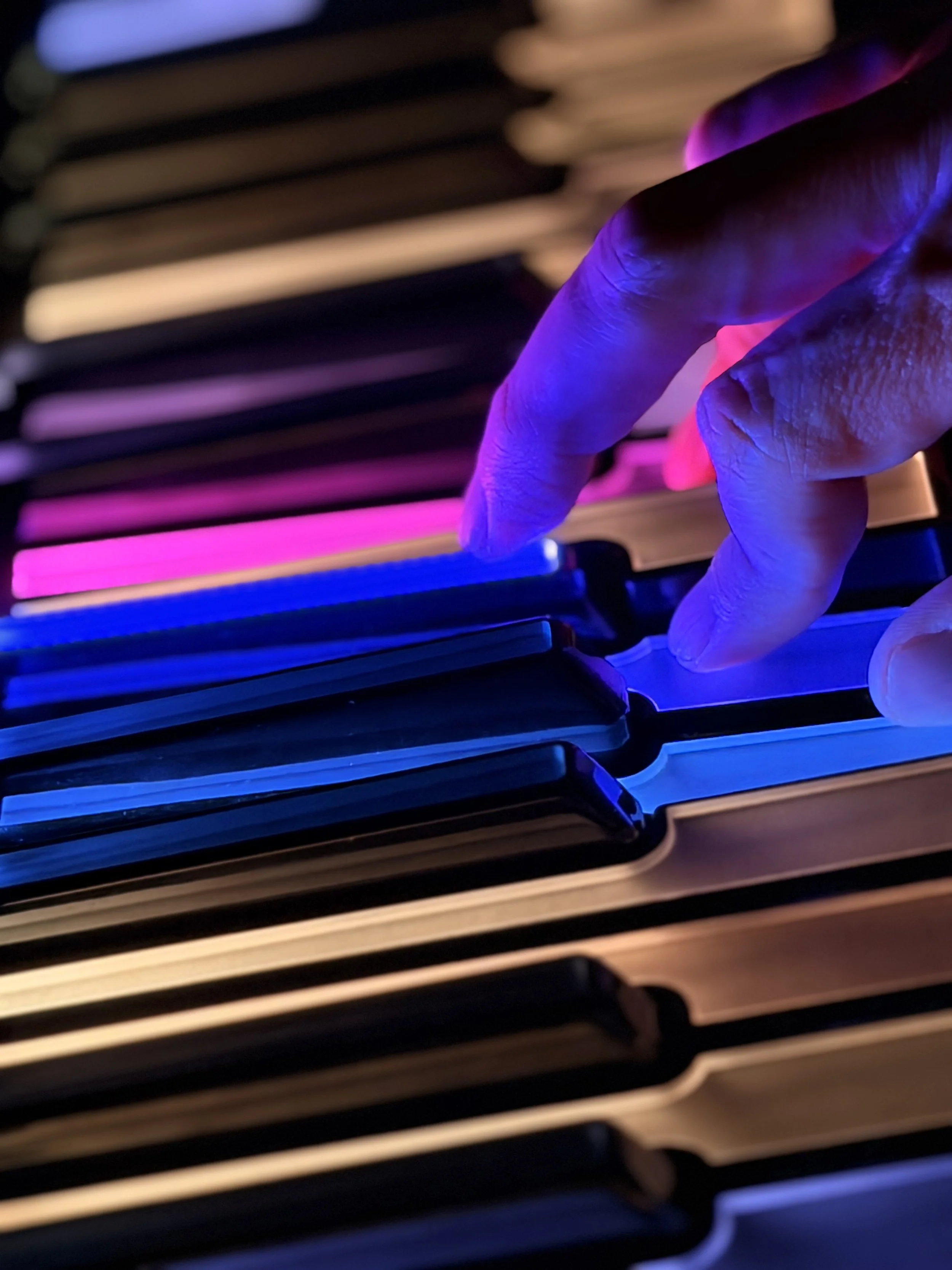 Tastiera di un computer con luci colorate blu, viola e rosa, e una mano che la tocca.