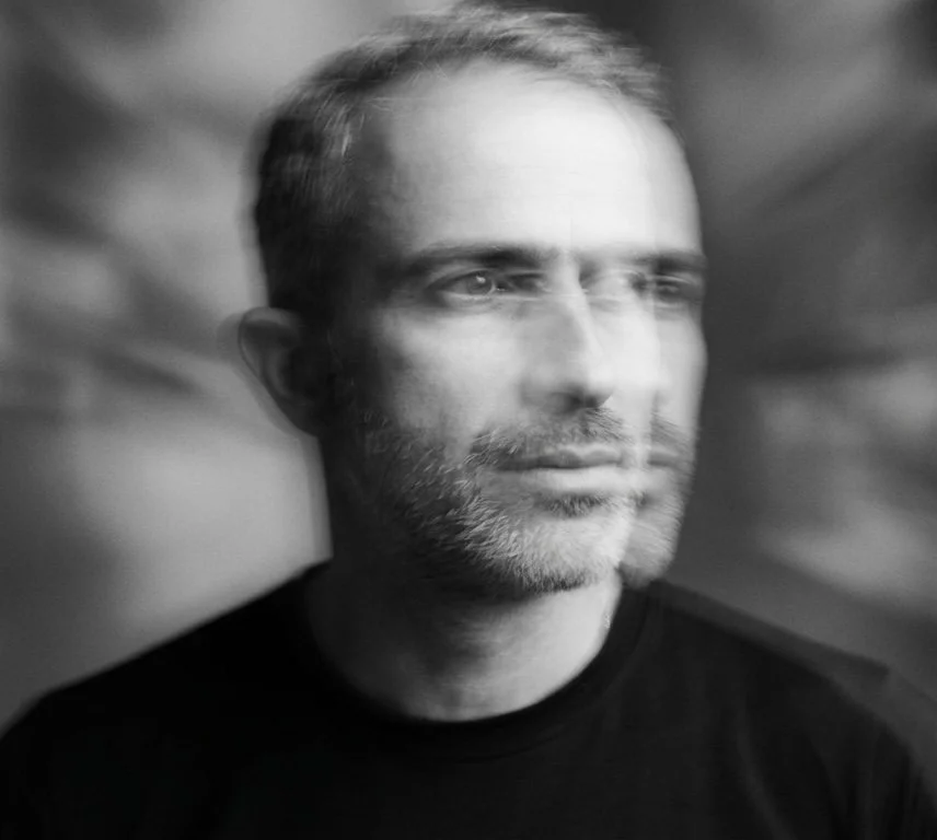 Ritratto di un uomo con barba e capelli corti, sfocato con effetto movimento, in bianco e nero.