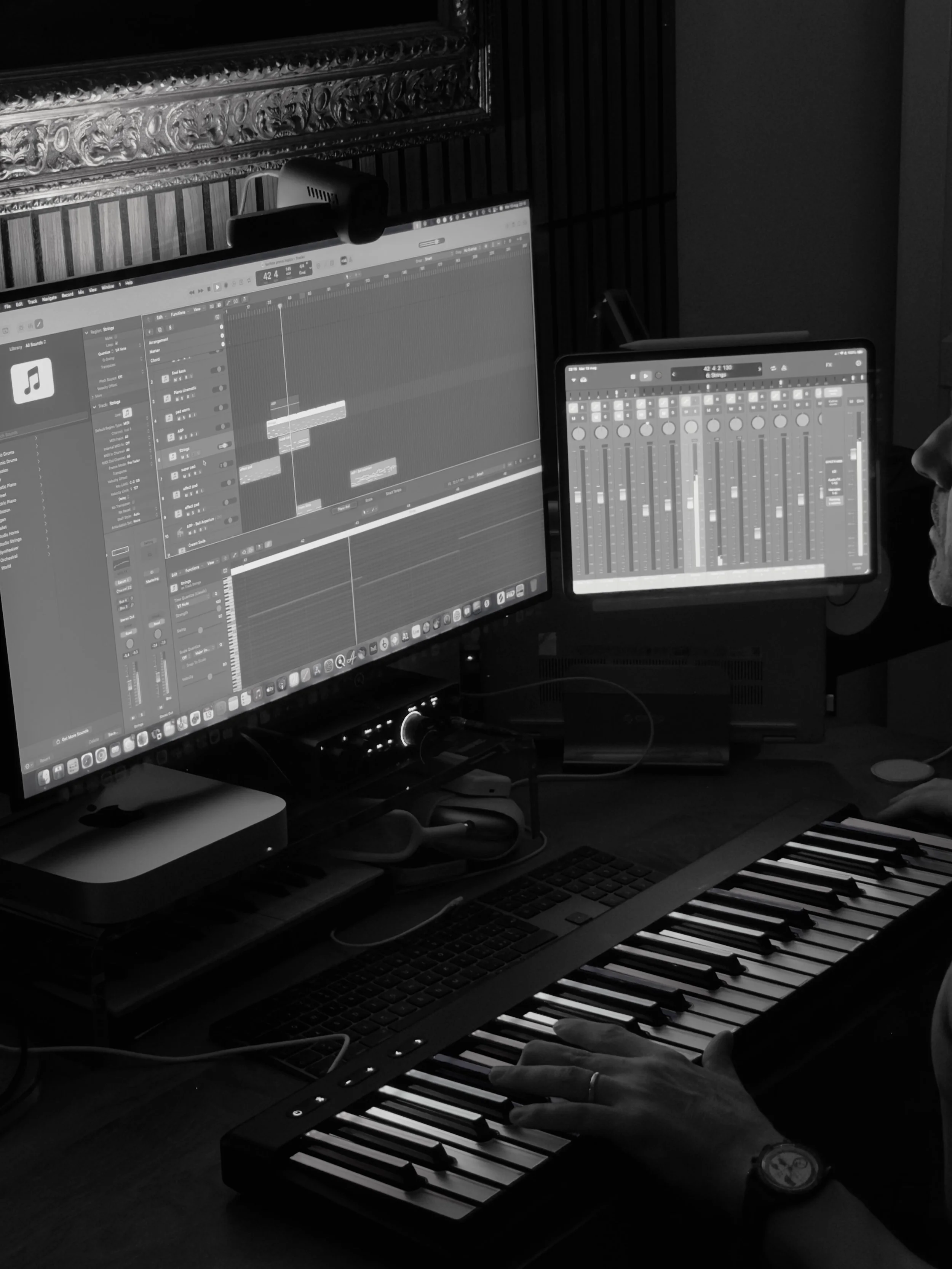Stanza di produzione musicale con due monitor, tastiera e controller MIDI, una mano che suona il controller, e una macchina fotografica sopra uno dei monitor.