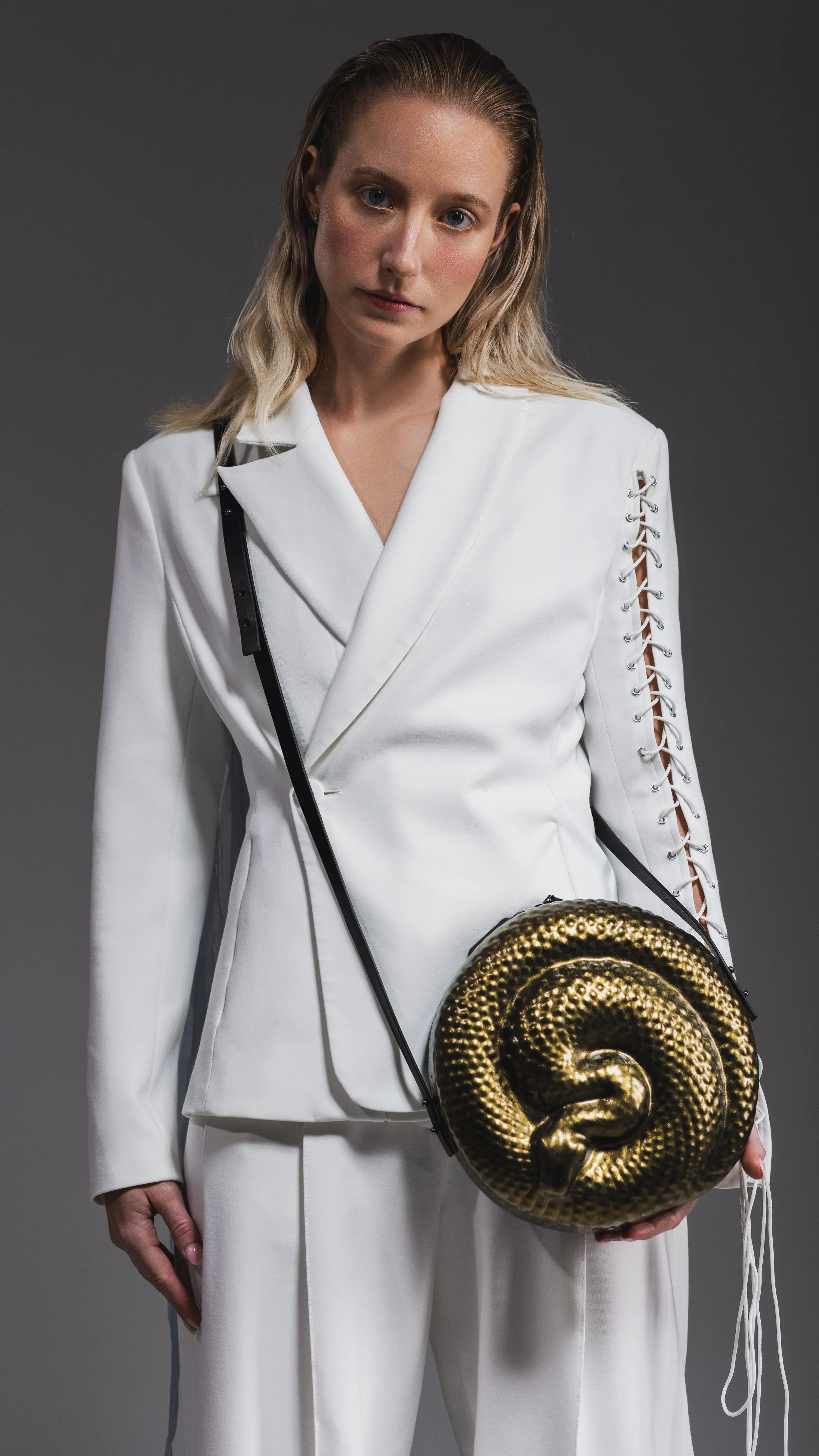A woman with blonde hair in a white suit holding a round black purse with a gold snake design