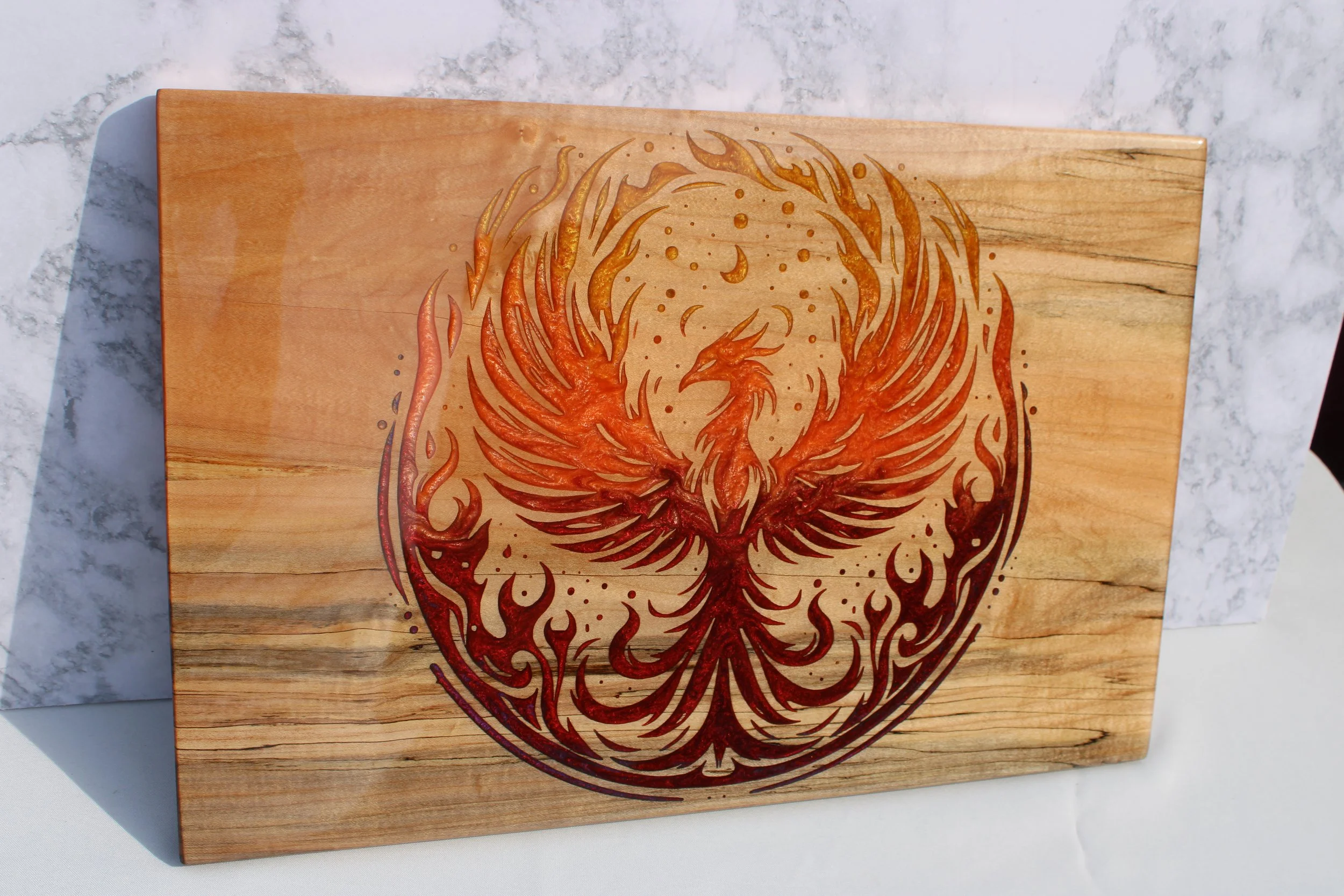 Wooden carving of a phoenix with flames, cut into a rectangular wooden board placed on a white marble surface.