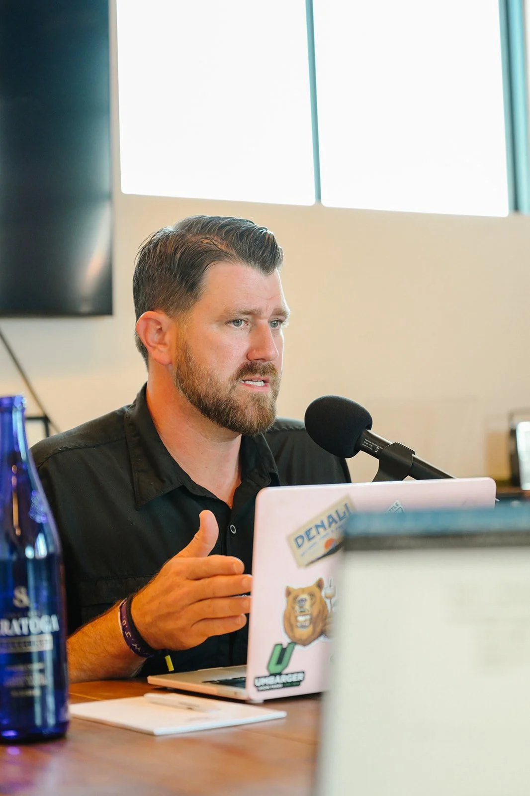 A man with dark hair and a beard speaking into a microphone during a podcast or radio recording about show lambs and show goats and how to raise them to be competitive show livestock projects