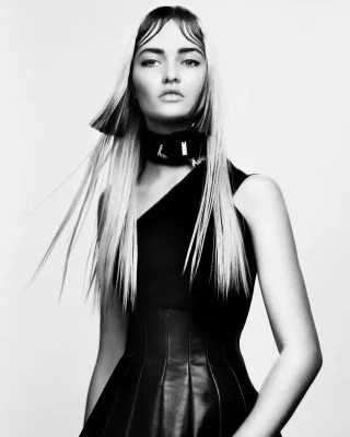 Black and white fashion portrait of a model with long straight hair, wearing a sleeveless black dress and a high collar.