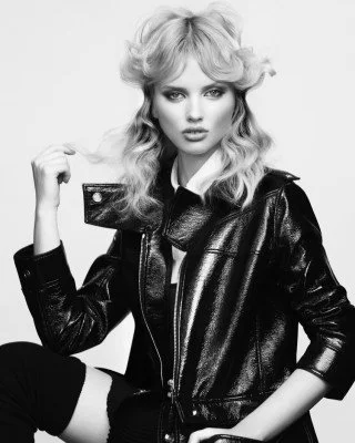 Black and white portrait of a stylish person with curly hair, wearing a leather jacket and a collared shirt.