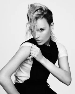 Person with edgy hairstyle wearing a sleeveless top and looking to the side in a black and white photo.