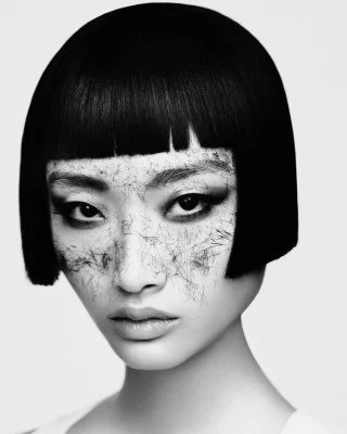 Black and white portrait of a person with short, straight black hair and artistic makeup on the face.