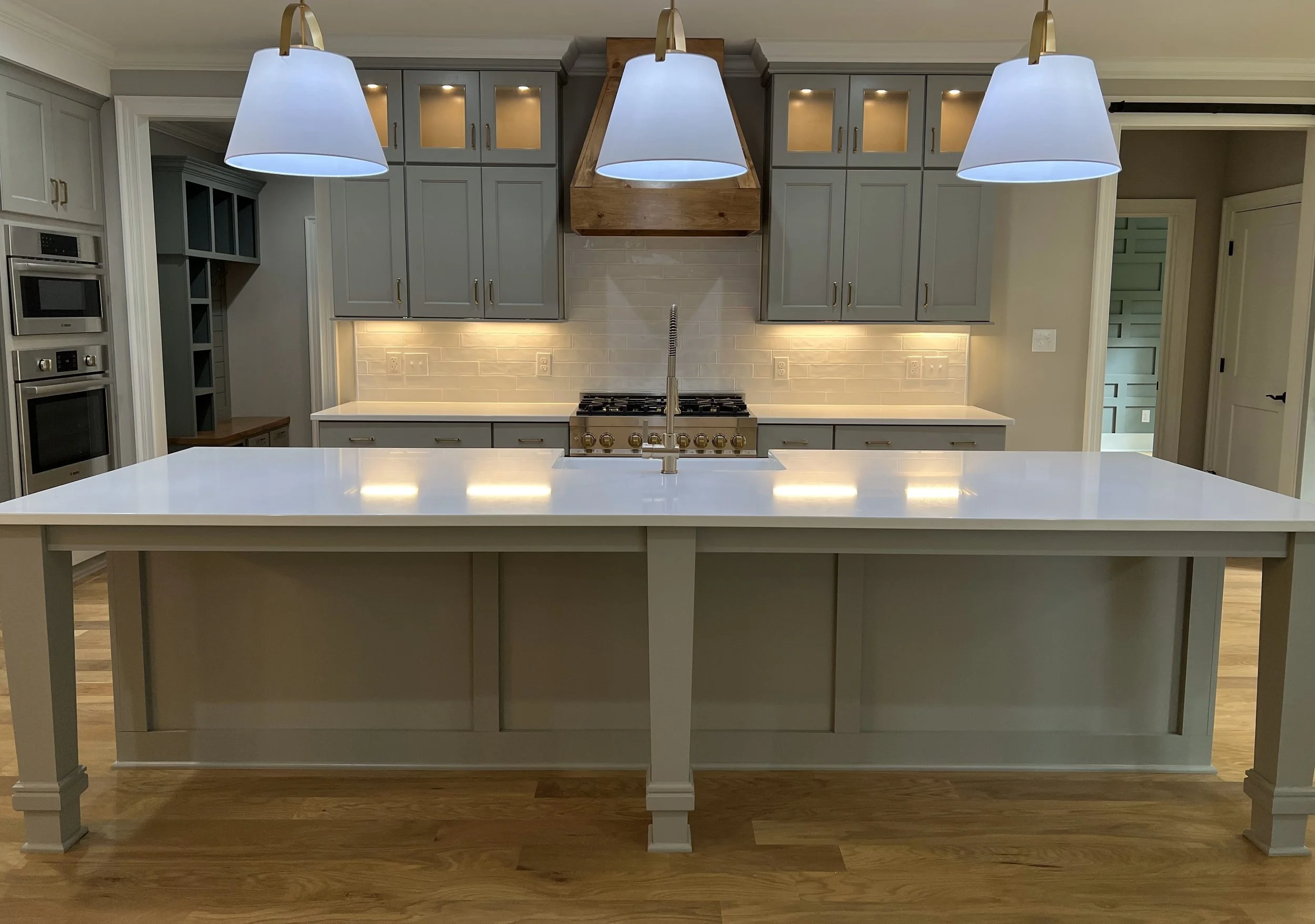 Modern kitchen with white island counter, gray cabinets, stainless steel stove, and hanging pendant lights.