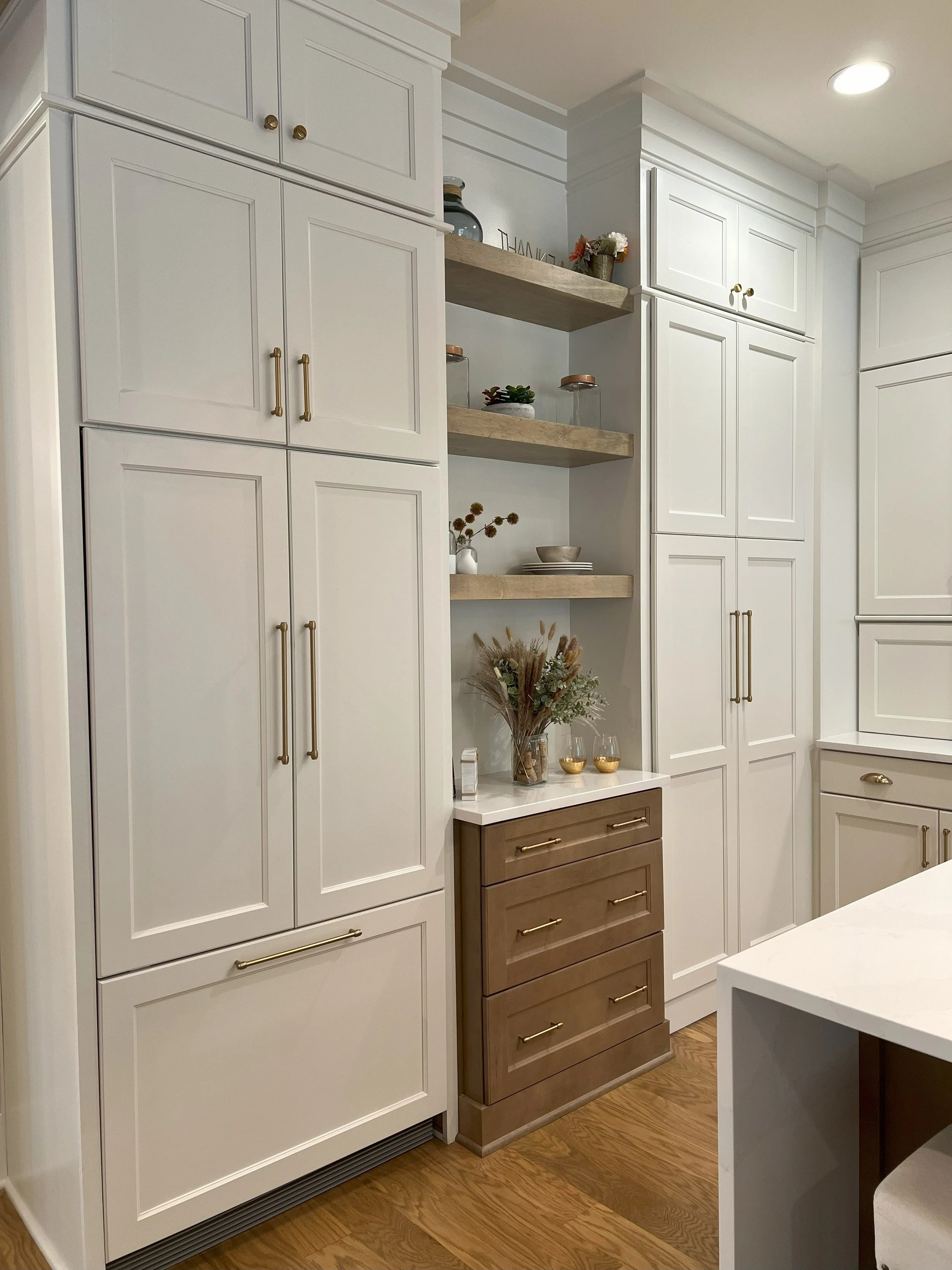 Kitchen with white cabinets, open shelves with decor, and a small wooden dresser with greenery and glassware.