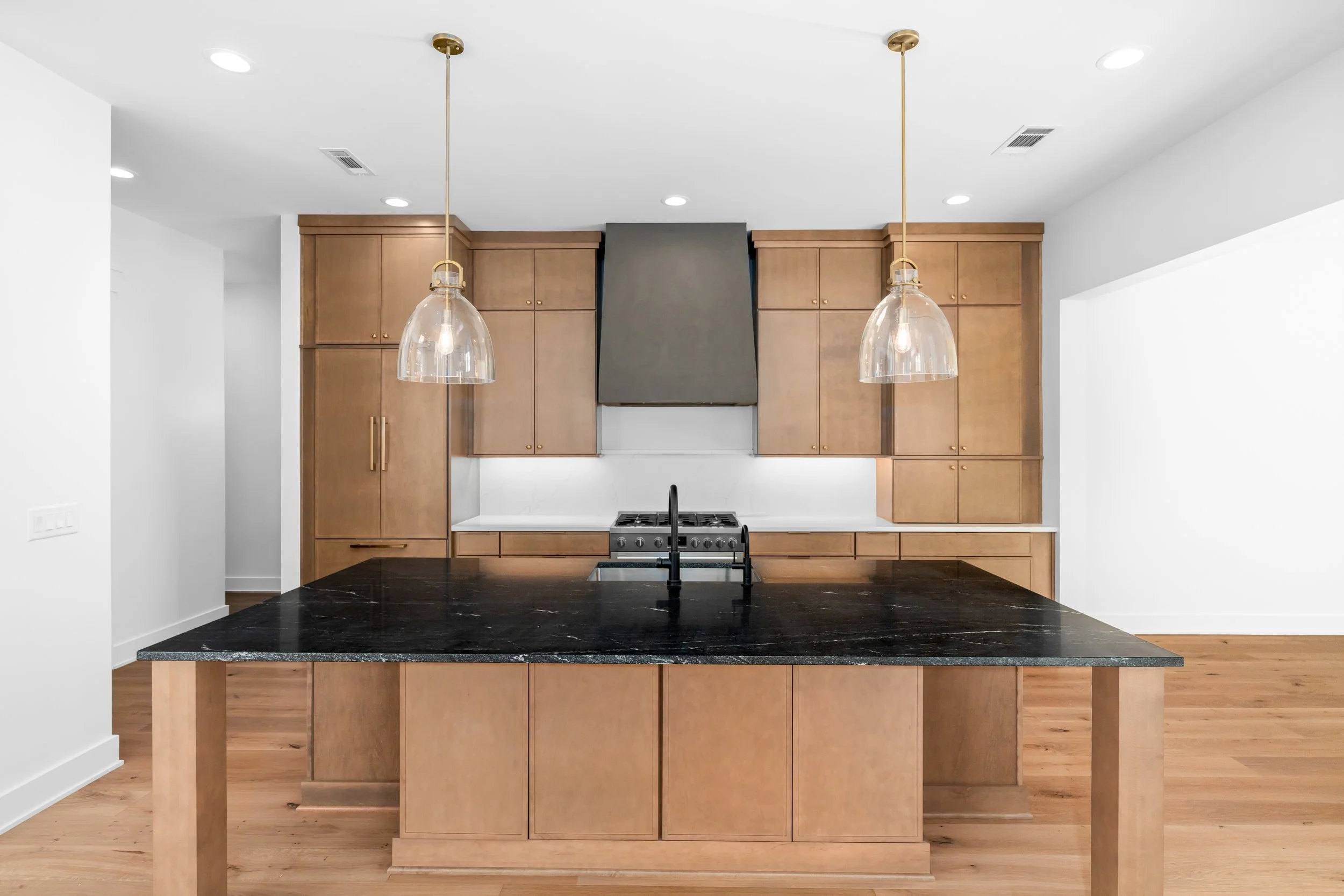 Modern kitchen with wooden cabinets, black countertop island, gray range hood, and pendant lights.