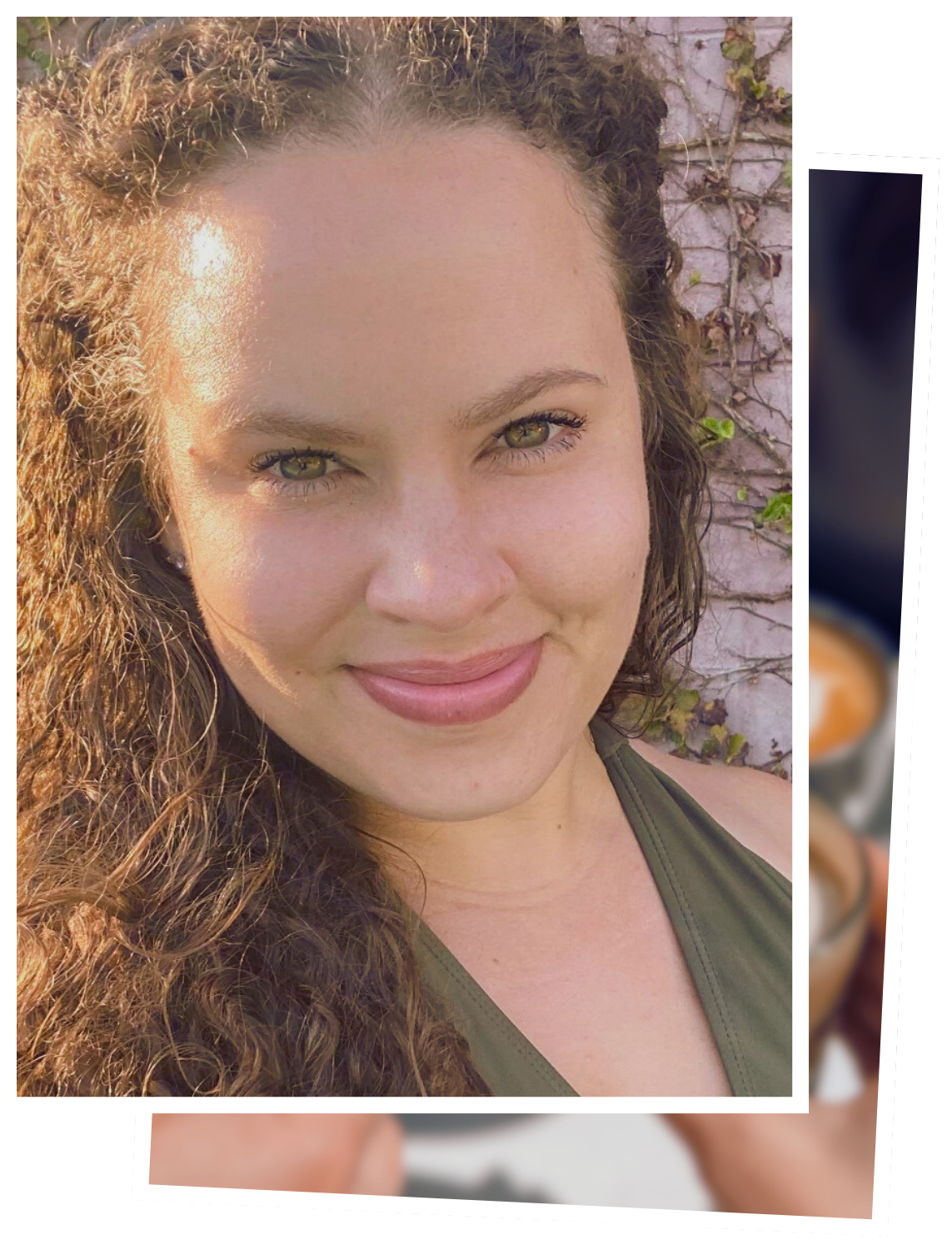 Close-up portrait of a young woman with curly brown hair, fair skin, and green eyes, smiling outdoors with sunlight on her face and a background of a vine-covered wall.