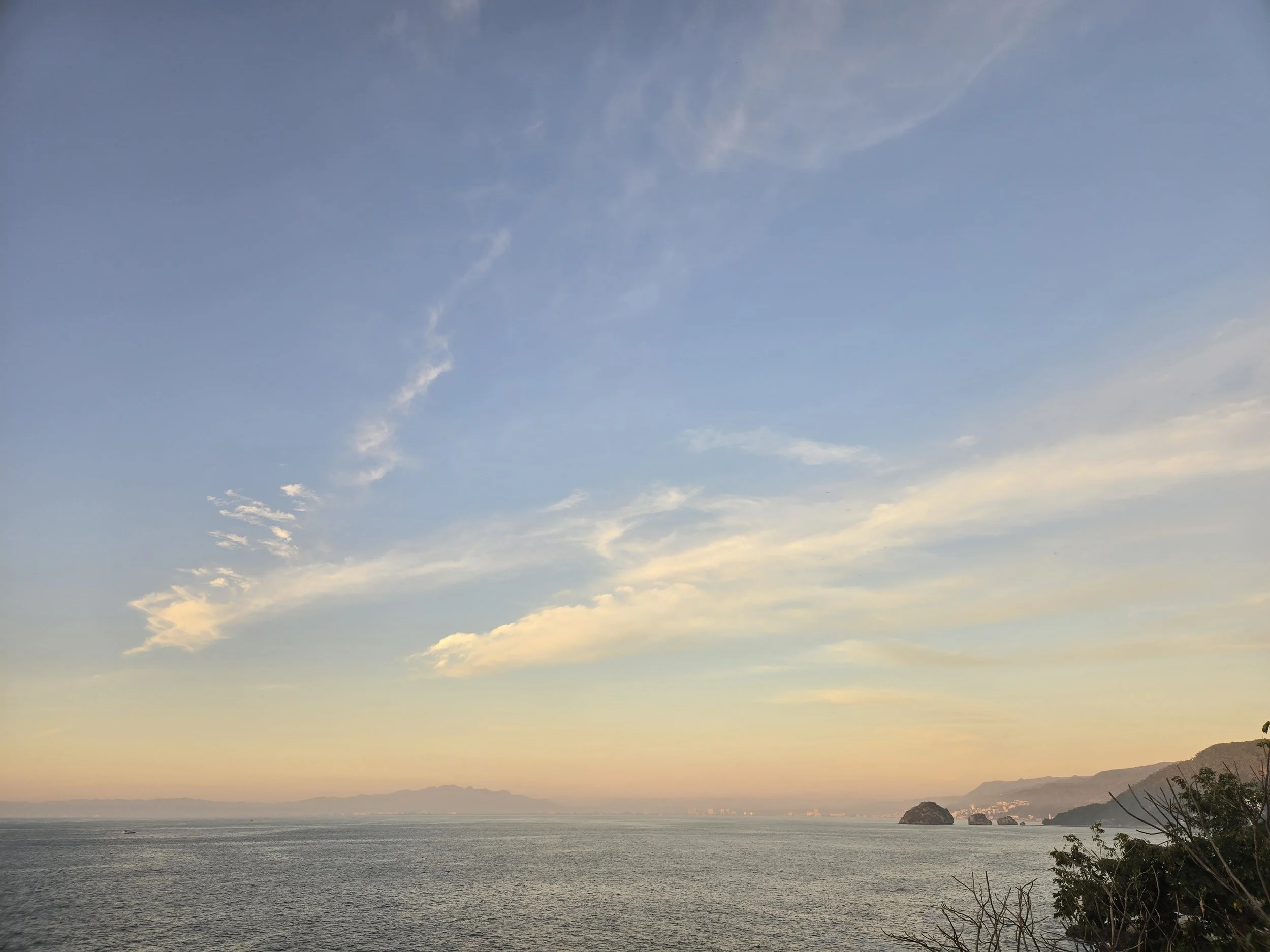 Ocean view during sunset with distant mountains and a partly cloudy sky.