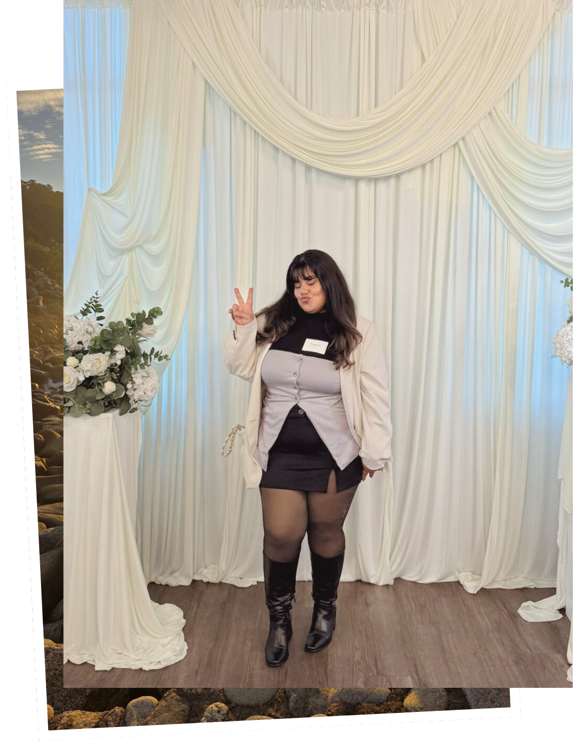 A woman with dark hair and bangs making a peace sign and puckering her lips, standing in front of white curtains with floral arrangements on either side, wearing a black turtleneck, beige blazer, gray button-up top, black mini skirt with slit, sheer black tights, and black knee-high boots.
