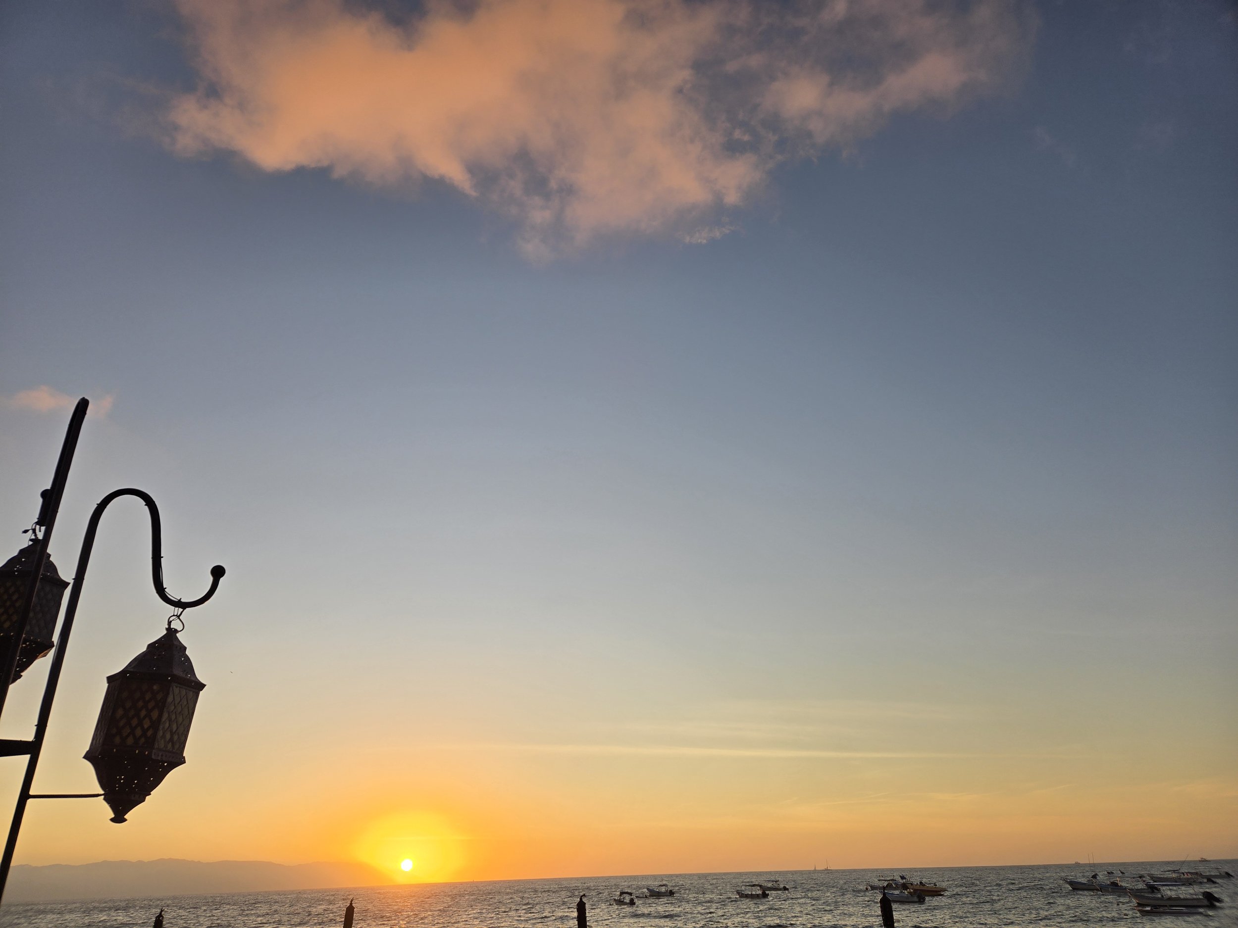 Sunset over the ocean with boats on the water and a light pole in the foreground.