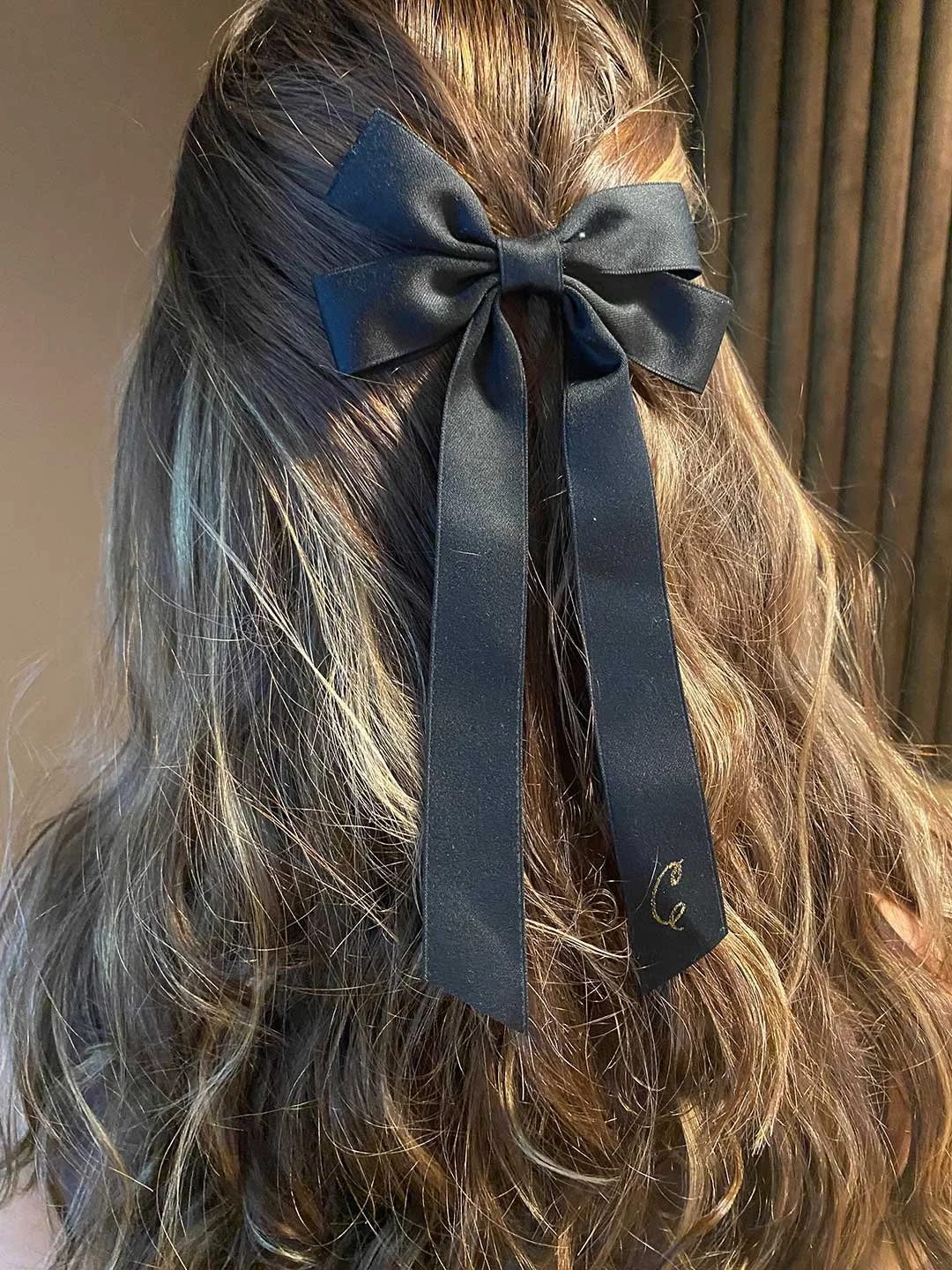 Close-up of a person with long, wavy blonde hair wearing a black satin bow tied at the back of their head.