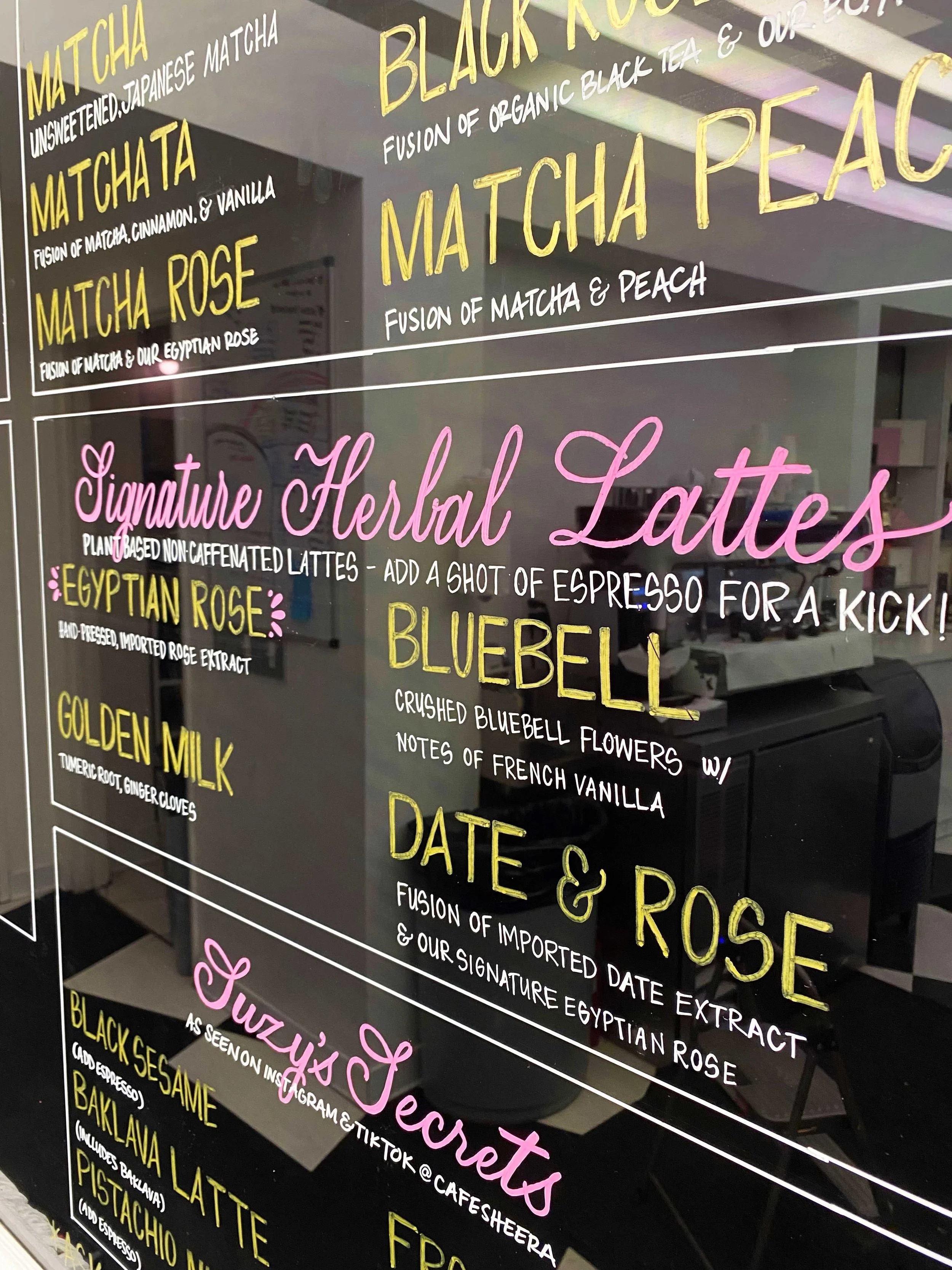 A menu board displaying various herbal latte options in colorful and decorative writing, including matcha, black rock, and peach, with descriptions and ingredients listed.