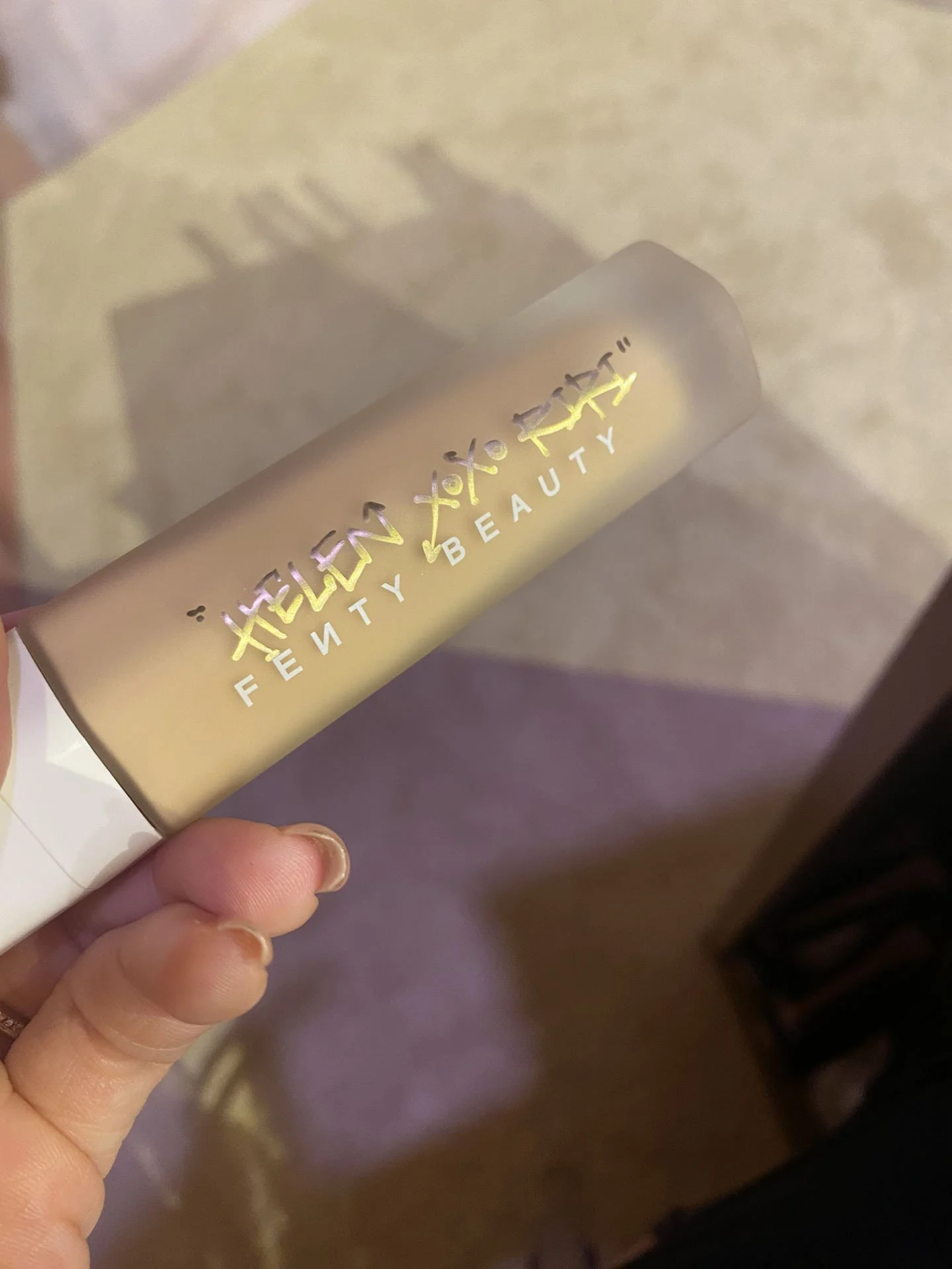 A hand holding a gold-colored tube of Fenty Beauty makeup.