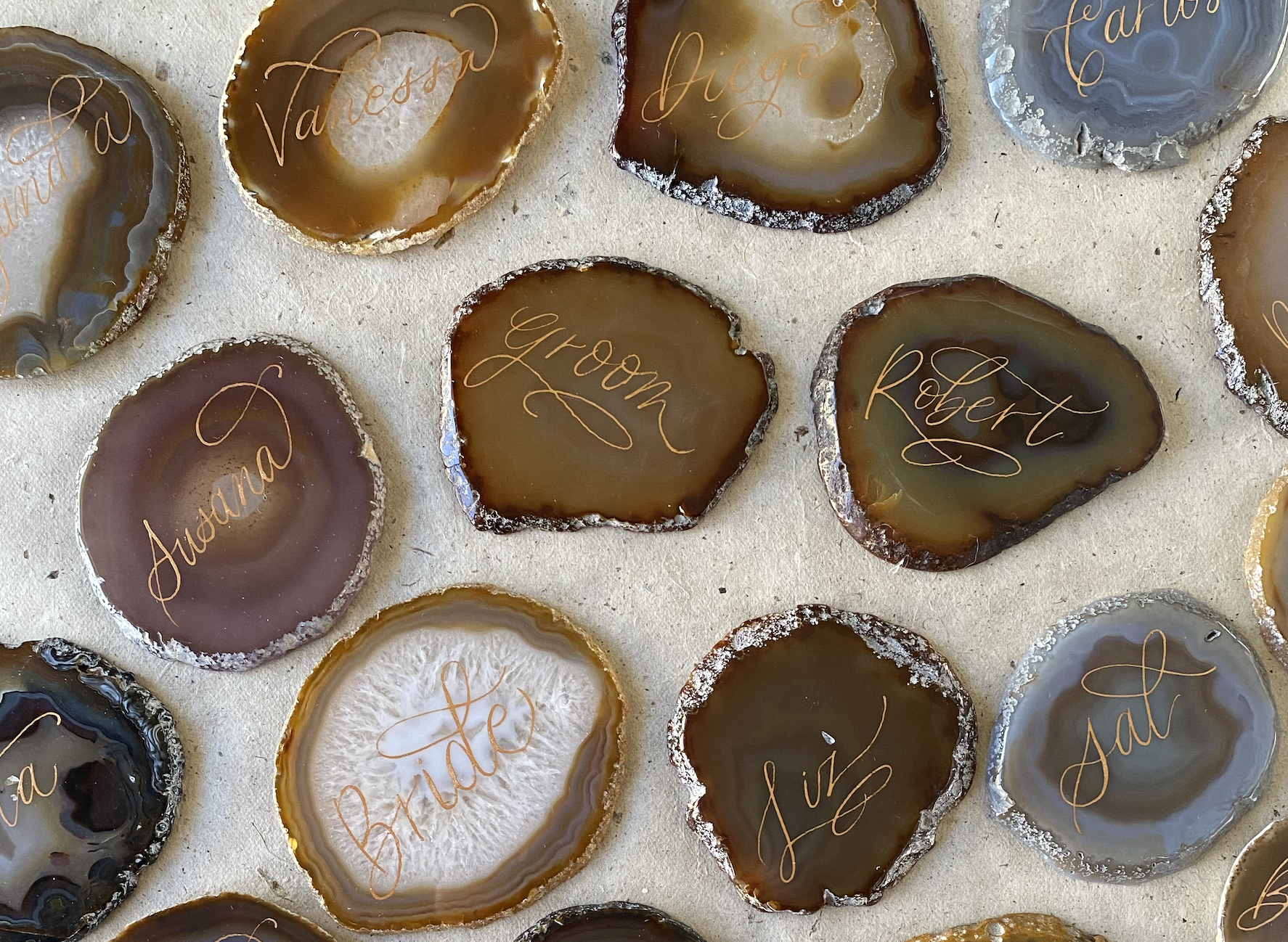 Multiple polished agate stones with handwritten names in orange ink, such as Vanessa, Groon, Robert, Aulana, and Jade, on a light-colored surface.