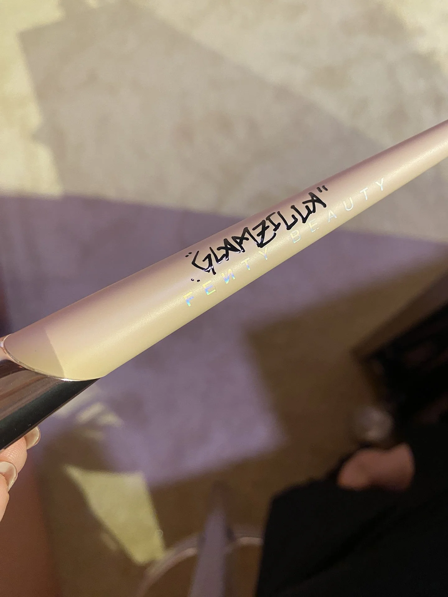 A Gillette Venus Beauty razor with a white handle and black text, held by a person with a light skin tone, with carpeted floor and person’s foot wearing a sandal in the background.