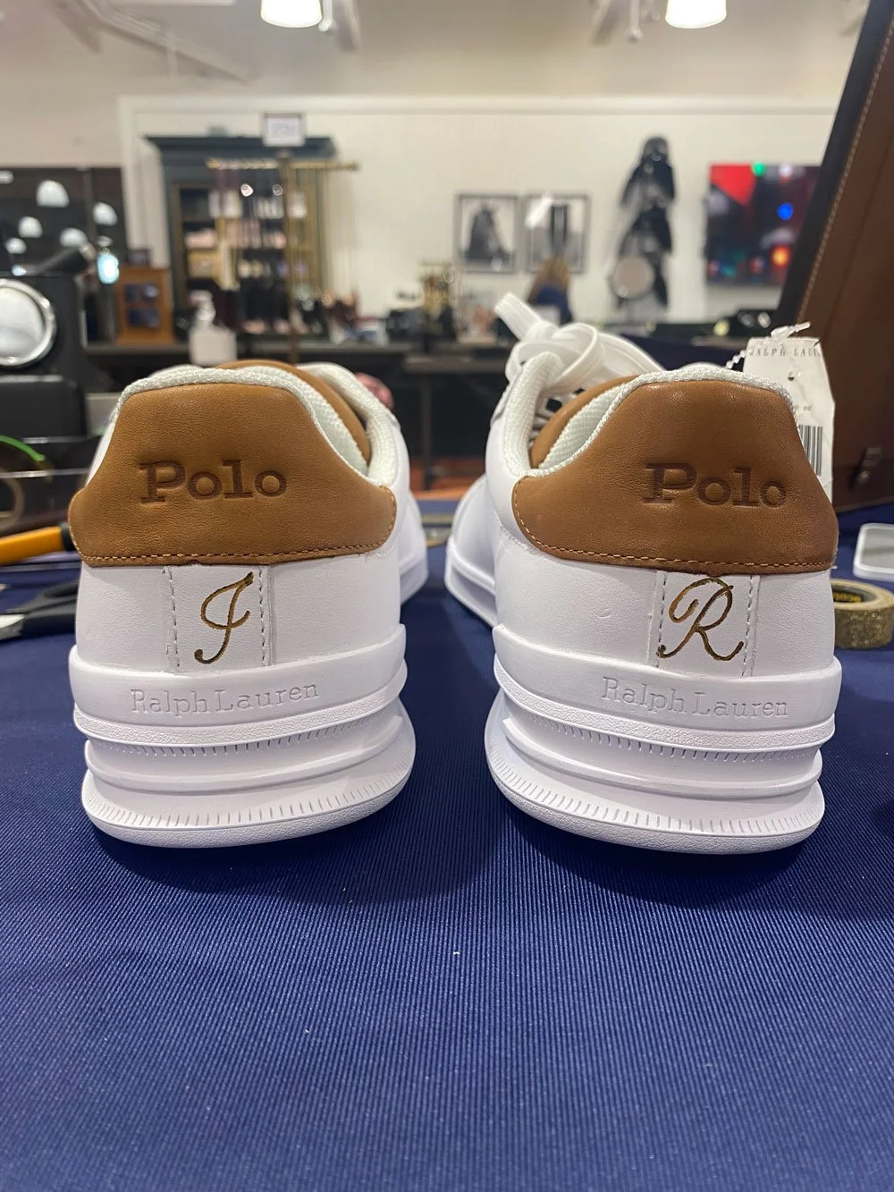 Pair of white Polo Ralph Lauren sneakers with tan accents, showing the back of the shoes with initials 'J' and 'R' and the brand name on the heel.