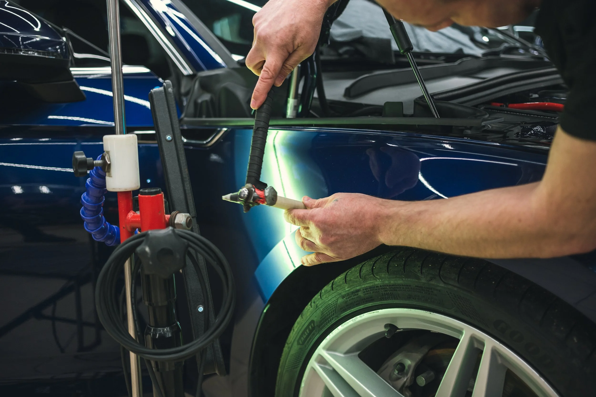 Technician using a paintless dent repair tool on a car door