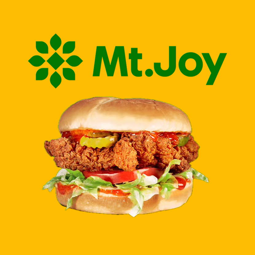 A fried chicken sandwich with lettuce, tomato, pickles, and sauce, with the text 'Mt. Joy' and a green geometric logo on a yellow background.