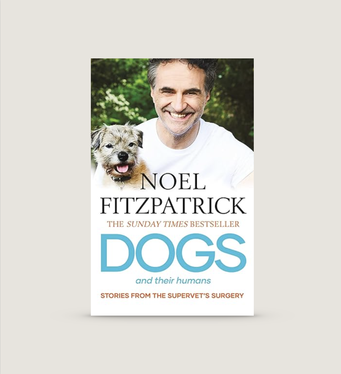 Book cover of 'Dogs and Their Humans' by Noel Fitzpatrick featuring a man smiling and holding a small dog, with greenery in the background.
