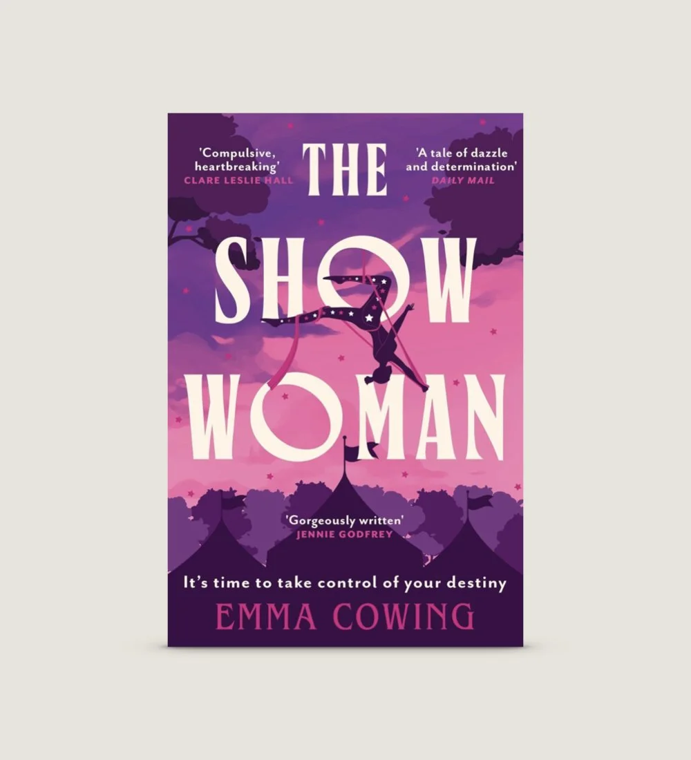 Book cover for 'The Show Woman' by Emma Cowing, featuring a silhouette of a woman performing a trapeze act against a pink and purple sky with circus tents at the bottom.