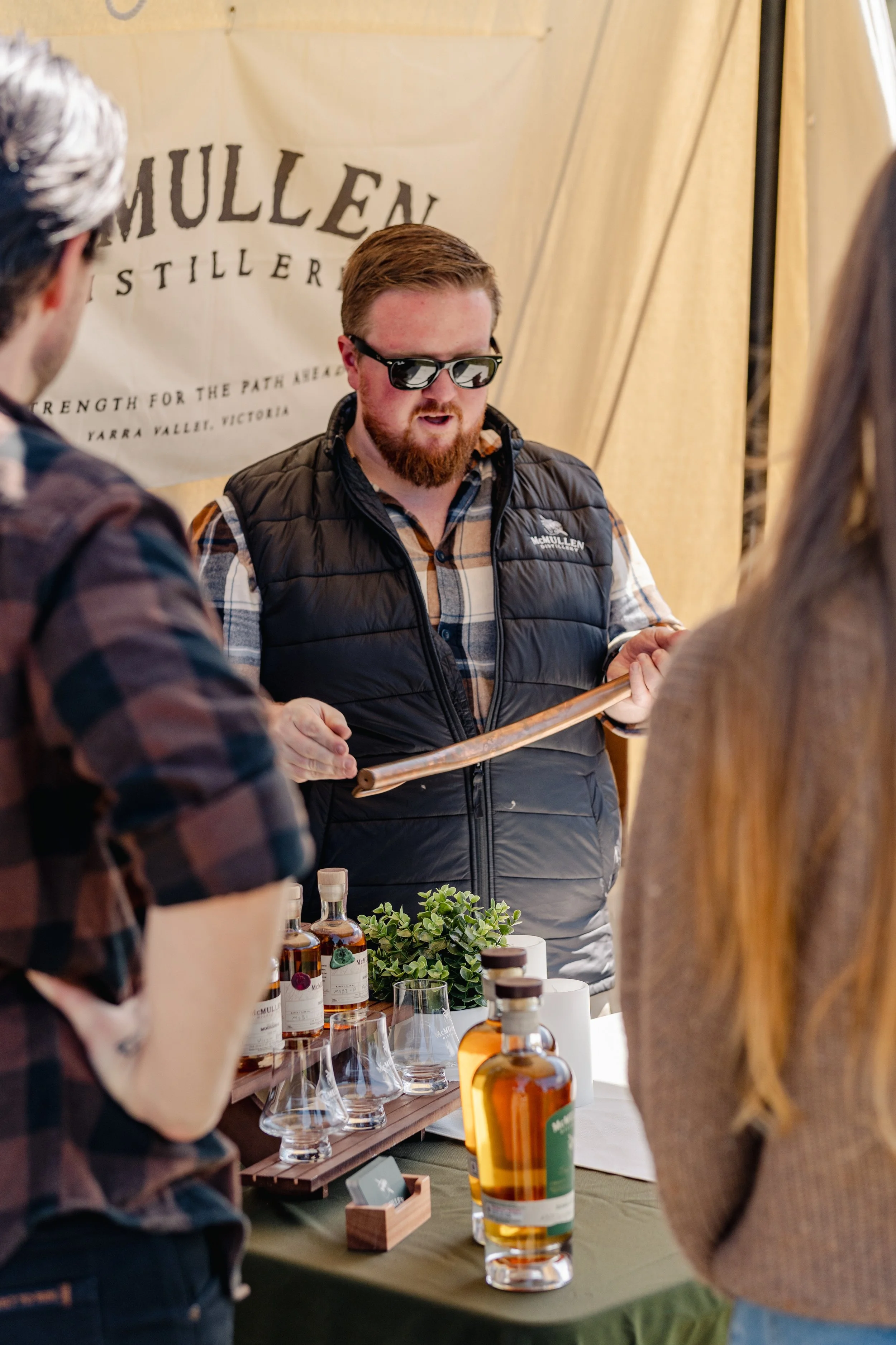Person tasting whiskey in a distillery setting with bottles and barrels in the background.