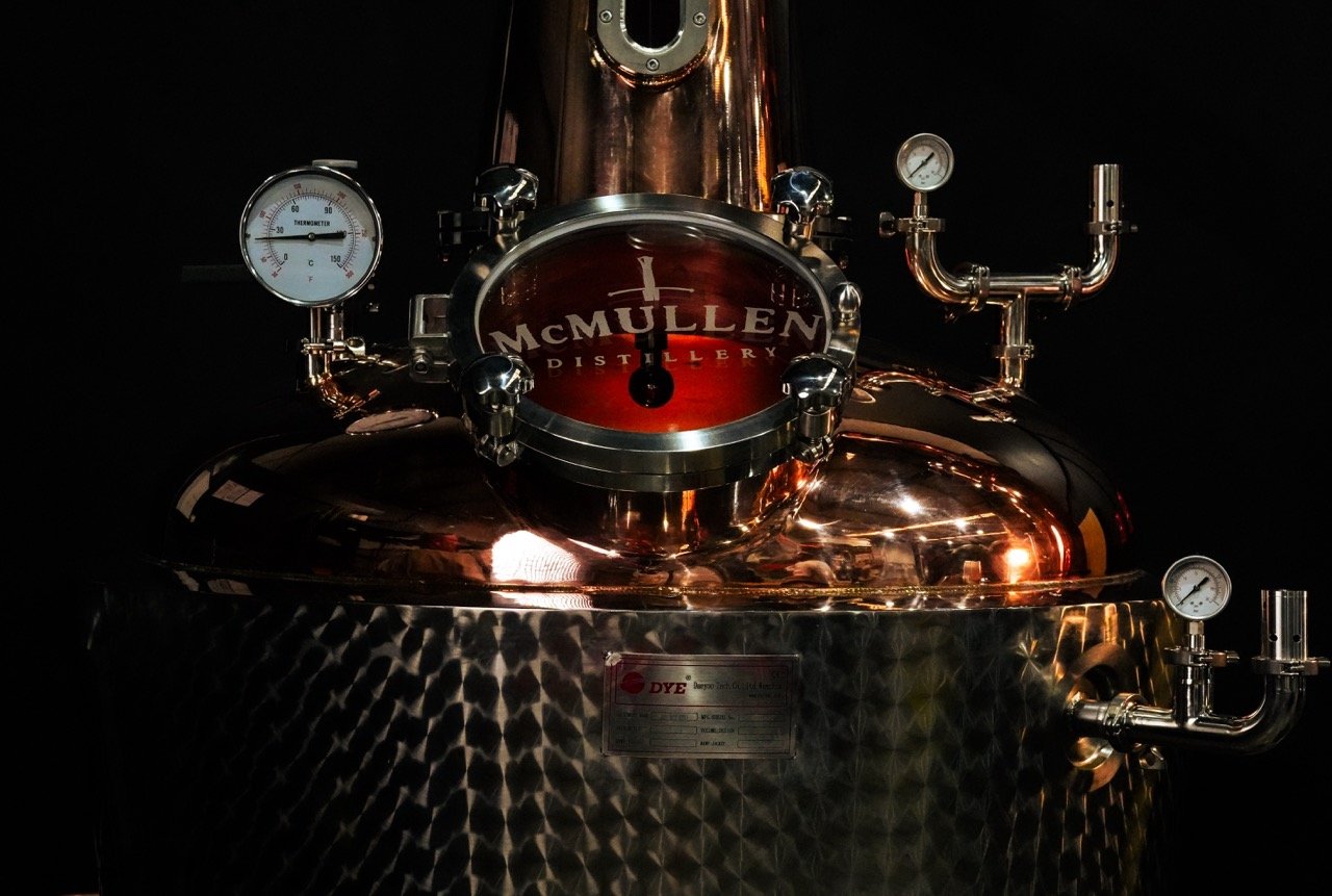A copper pot still, featuring McMullen Distillery branding.