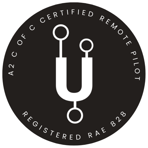 Circular logo with a stylized white U-shaped antenna symbol in the center, surrounded by text that reads 'A2C Certified Remote Pilot' at the top and 'Registered RAE 828' at the bottom on a black background.